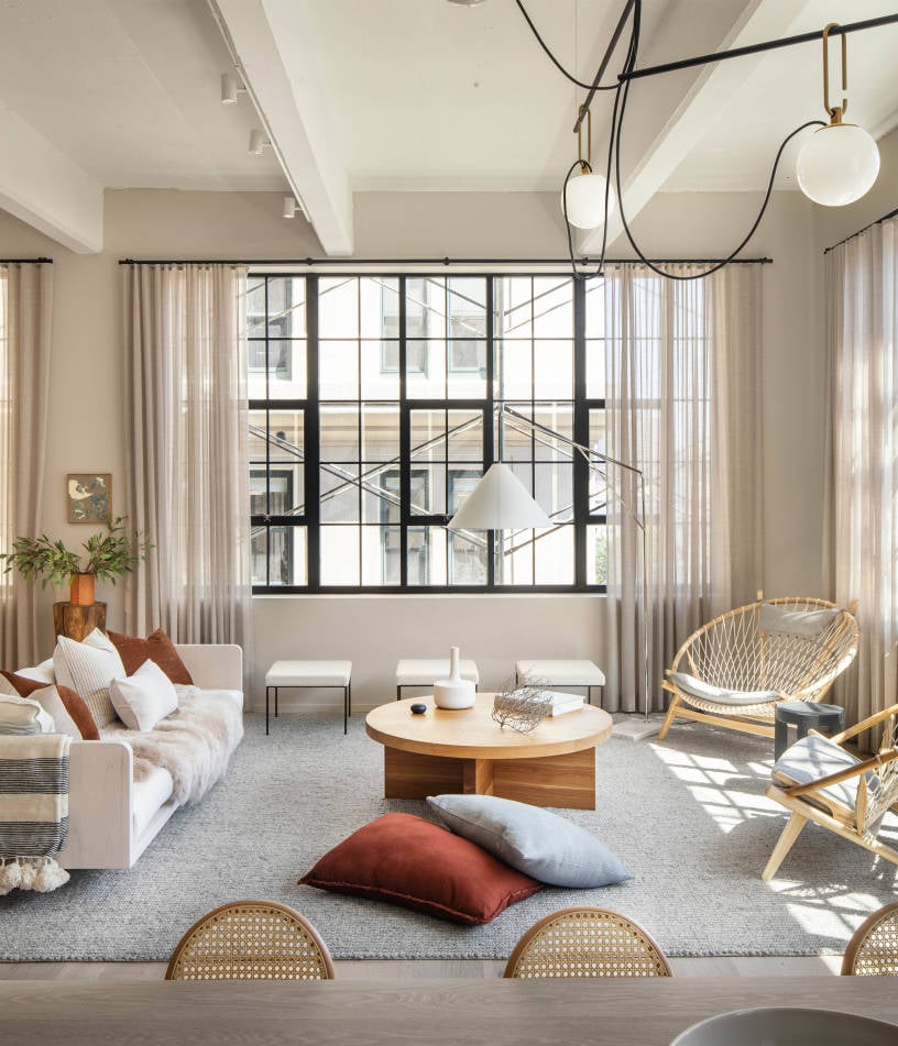 168 Plymouth, North America — Modern loft living room with black-gridded windows, natural light, wood coffee table, woven chairs, cream furnishings, and contemporary pendant lighting.