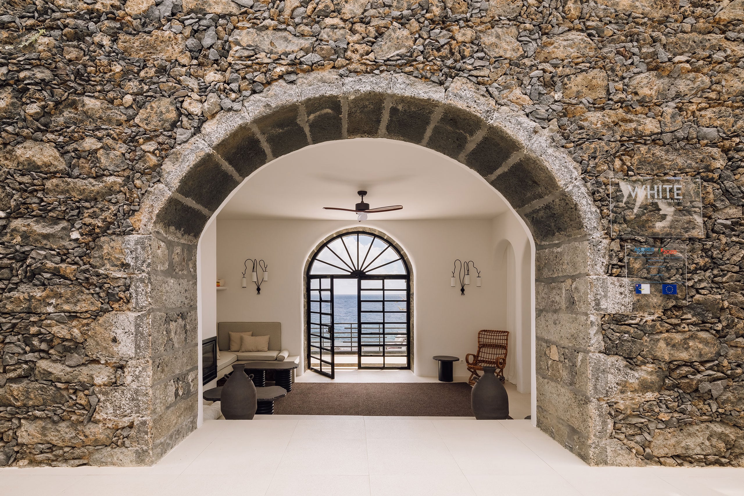 White Hotel, Europe — Arched stone passageway framing minimalist interior with sea-view doors, coastal luxury hospitality design.