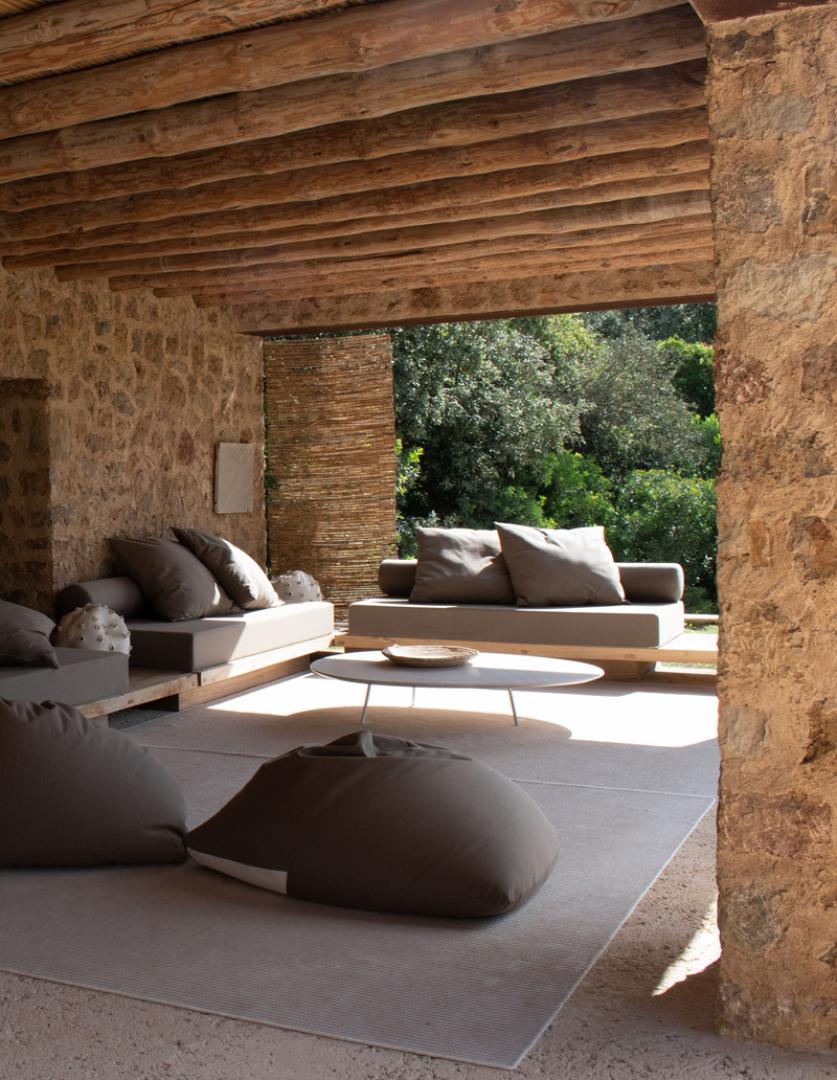Es Racó d'Artà, Balearic Islands — Stone pavilion with exposed timber beams, modernist furniture, and garden views through open colonnade.
