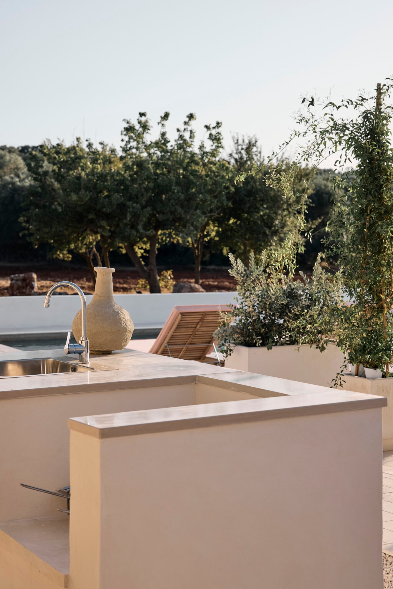 Villa Sessana, Italy — Minimalist outdoor kitchen with white stone countertop and faucet overlooking olive grove landscape in golden afternoon light.