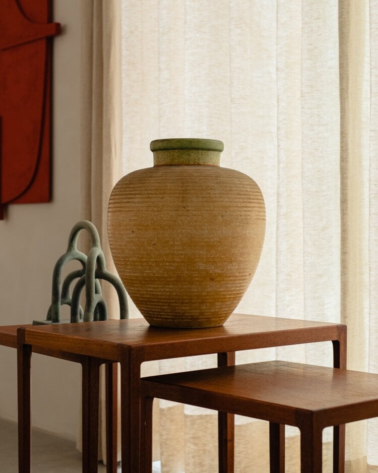 The Audo, Europe — Handcrafted ceramic vessel and sculptural decor on mid-century wooden side table with sheer curtains and minimalist interior styling.
