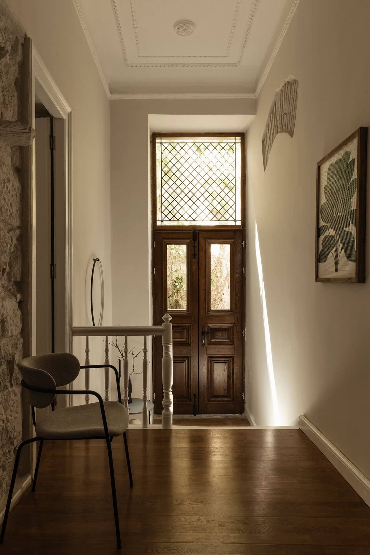 Casa Somos Suenos, Europe — Narrow hallway with cream walls, dark wood flooring, antique doors, natural light, botanical art, and modern chair.