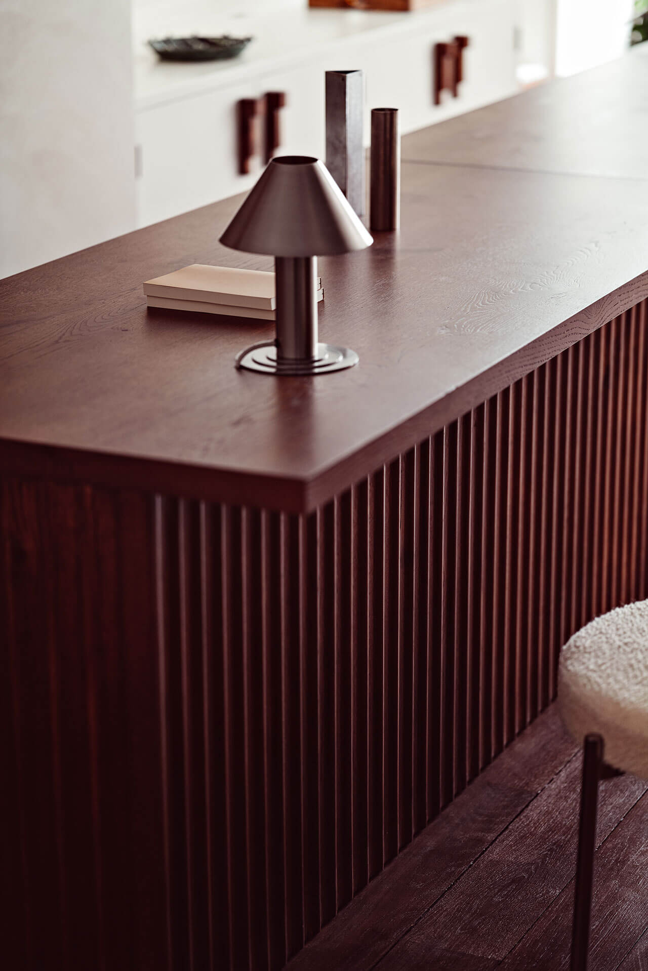 Académies et des Arts, Europe — Burgundy table with vertical fluted base, cone lamp, minimalist decor, warm natural light, modern luxury interior design.