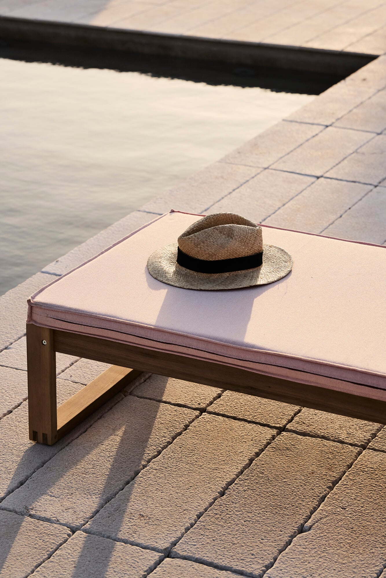 Villa Sessana, Italy — Straw hat with black band resting on cream lounger beside tiled poolside terrace and water, morning light casting sharp shadows.