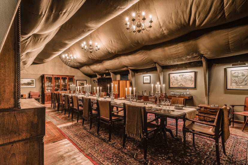 Zannier Sonop, Africa — Candlelit dining tent with draped cream fabric ceiling, wooden furnishings, oriental rugs, and vintage maps on canvas walls.