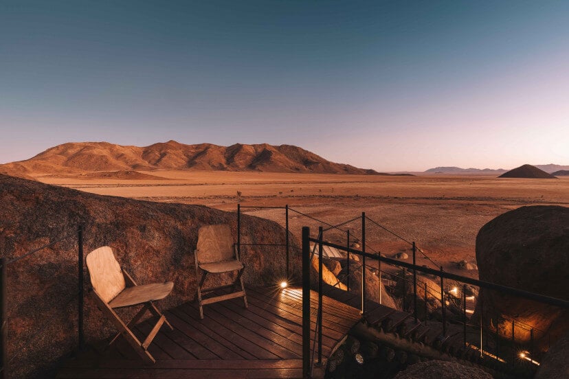 Zannier Sonop, Africa — Wooden deck with canvas chairs overlooking desert mountains at golden hour, luxury safari lodge architecture.