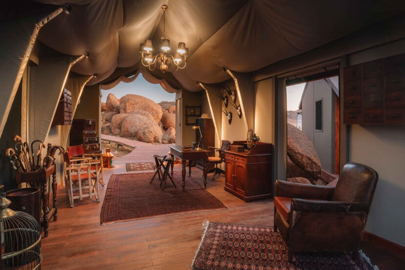 Zannier Sonop, Africa — Luxe canvas glamping tent interior with wooden floors, vintage furnishings, chandelier, and panoramic boulder landscape views.
