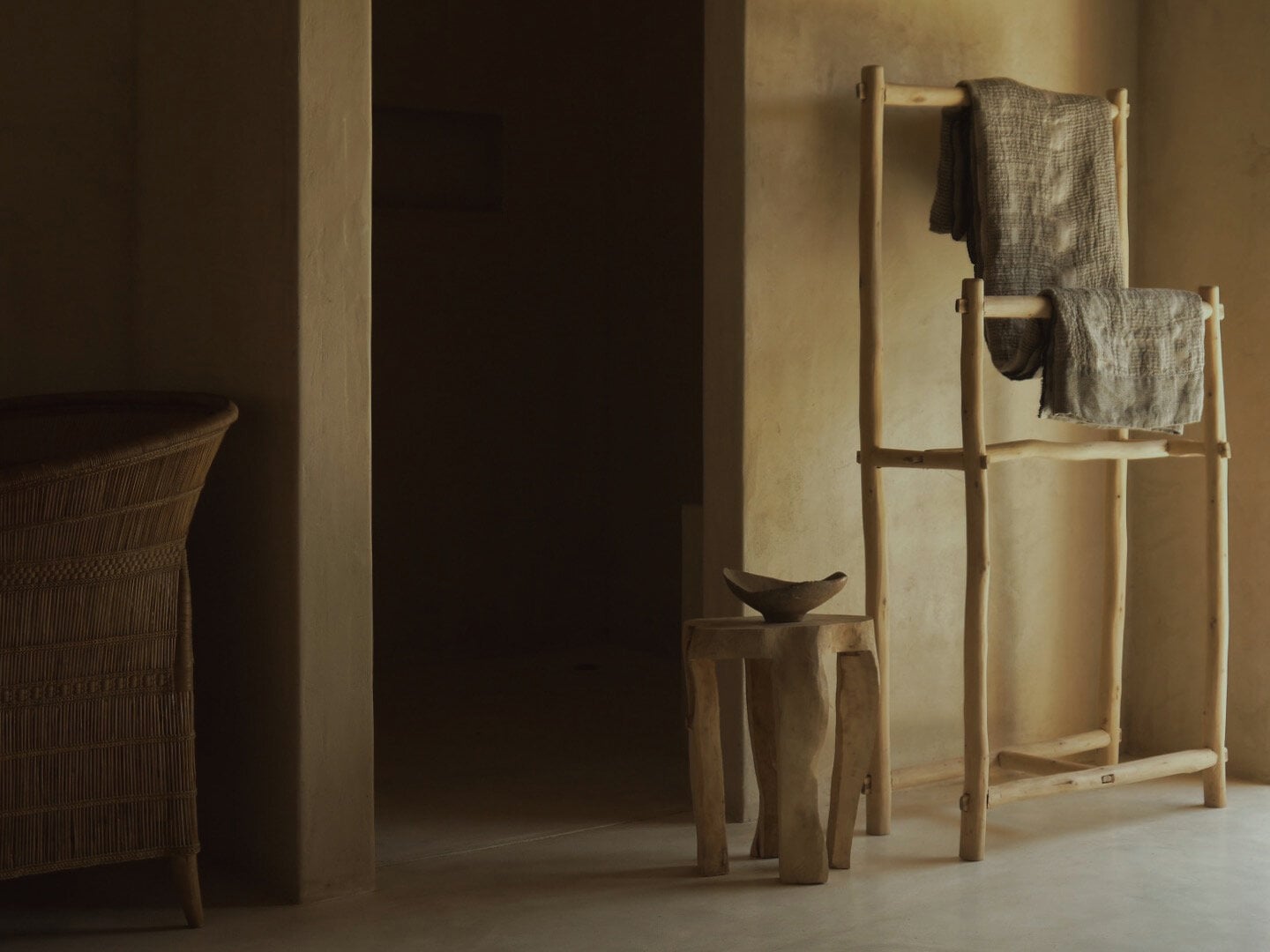 Sussurro, Africa — Minimalist bathroom with natural wood ladder shelf, linen textiles, ceramic vessel, woven chair, warm earth tones and soft directional light.