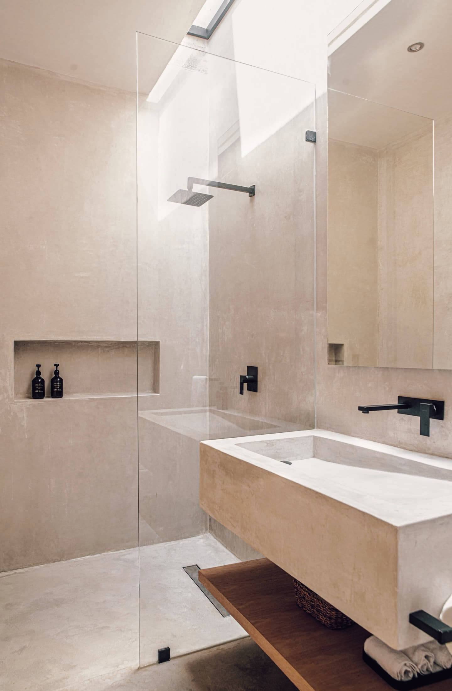 Villa Cava, Mexico — Minimalist bathroom with natural stone walls, floating vanity, frameless glass shower enclosure, and skylight flooding space with diffused light.