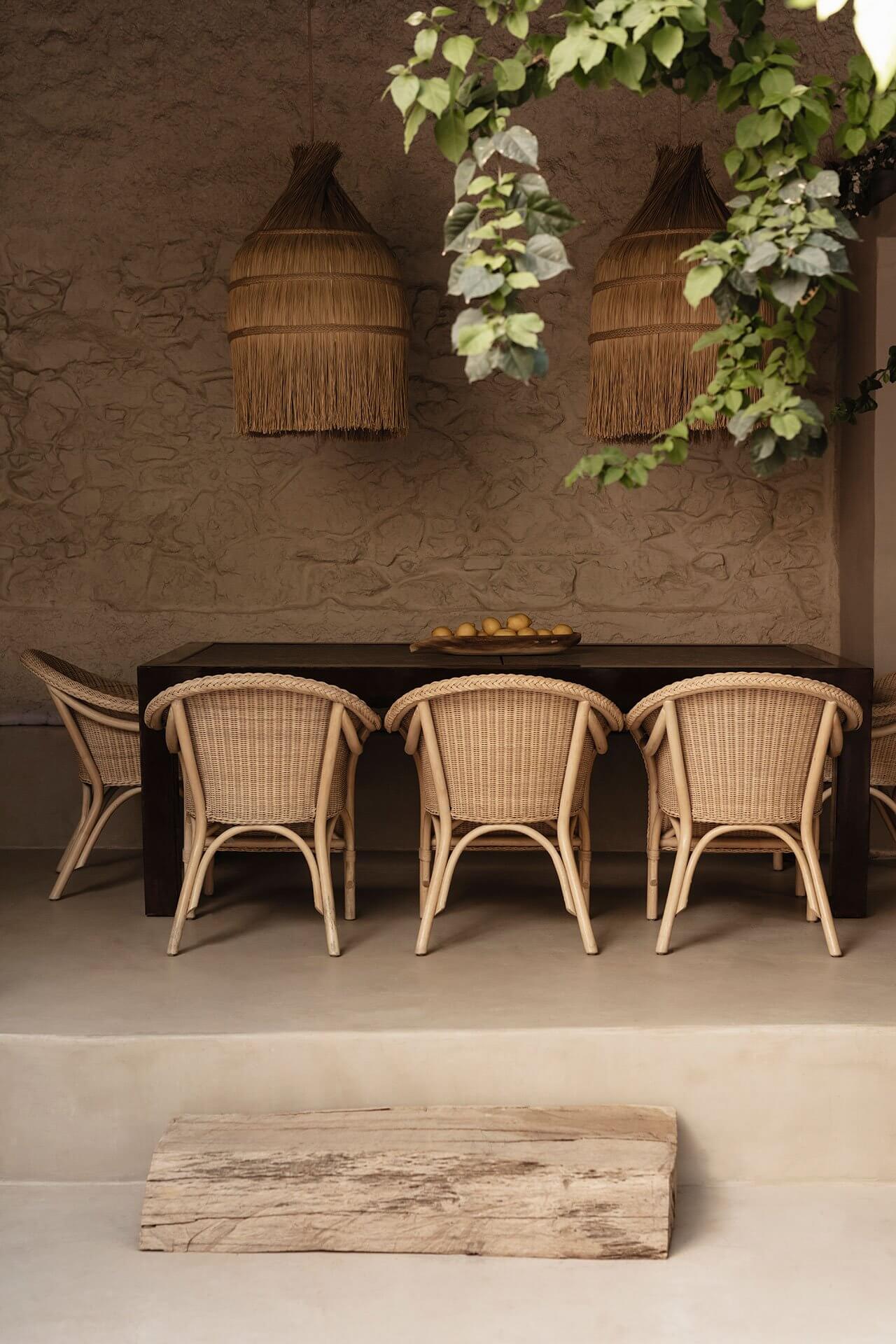 Casa Somos Suenos, Europe — Minimalist dining alcove with woven rattan chairs, black table, textured terracotta wall, and cascading ivy beneath pendant lamps.