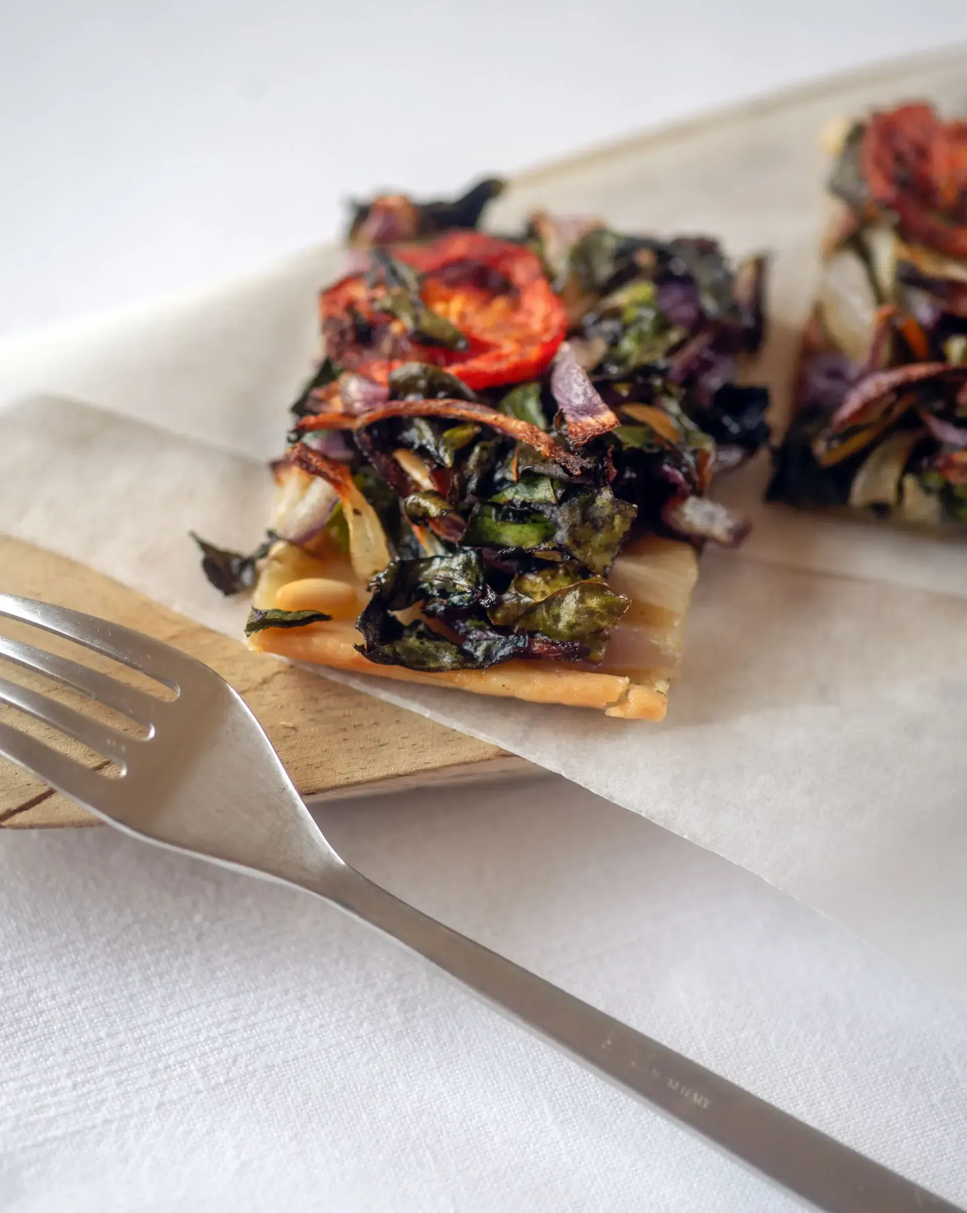 Es Racó d'Artà, Balearic Islands, Spain — Charred leafy greens and roasted vegetables on crisp crackers, plated on parchment with minimalist dining presentation.