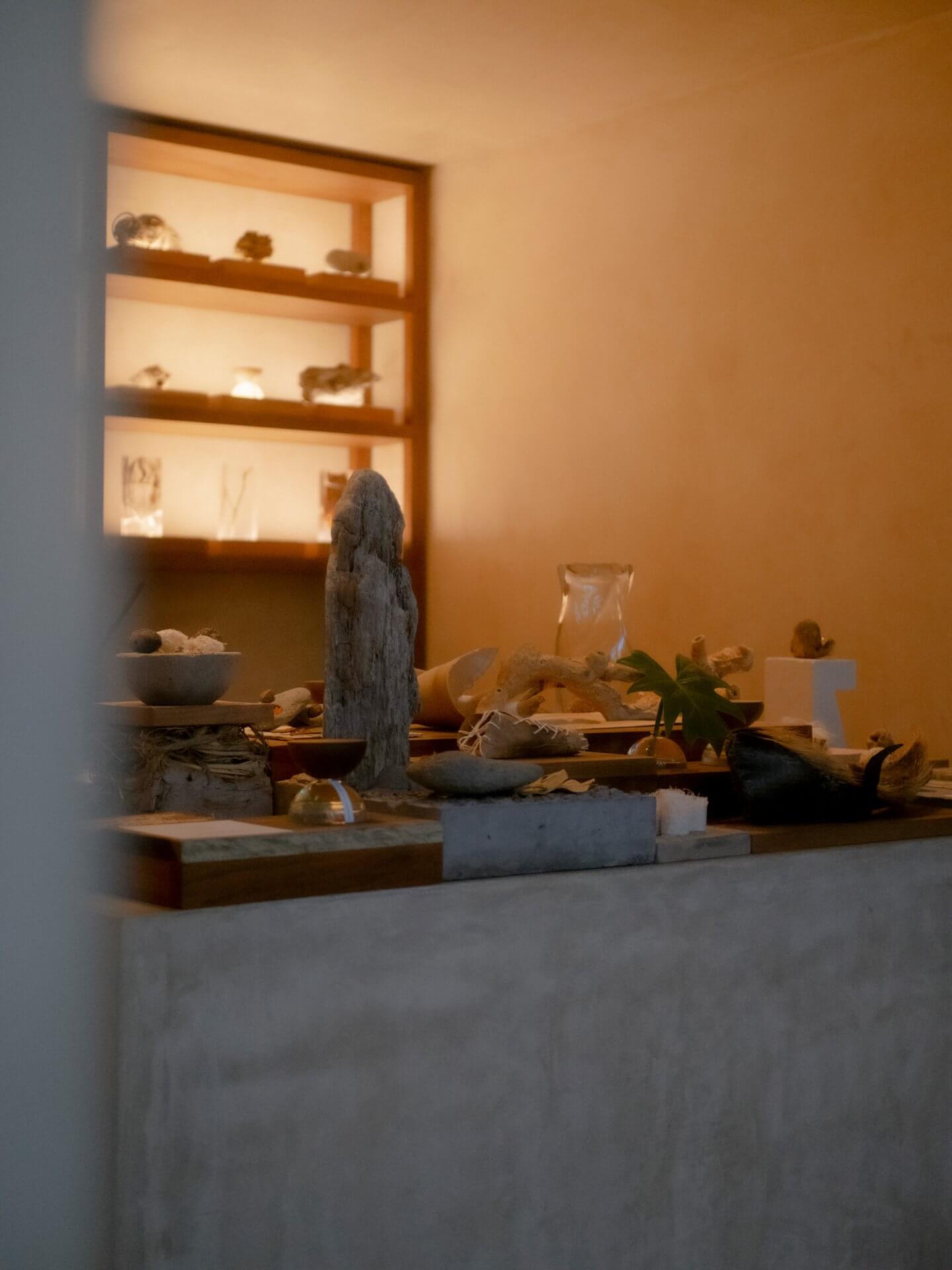 Xinú Perfumery, Mexico — Minimalist retail display with stone sculptural forms, warm ambient lighting, and wooden shelf niche housing curated objects.