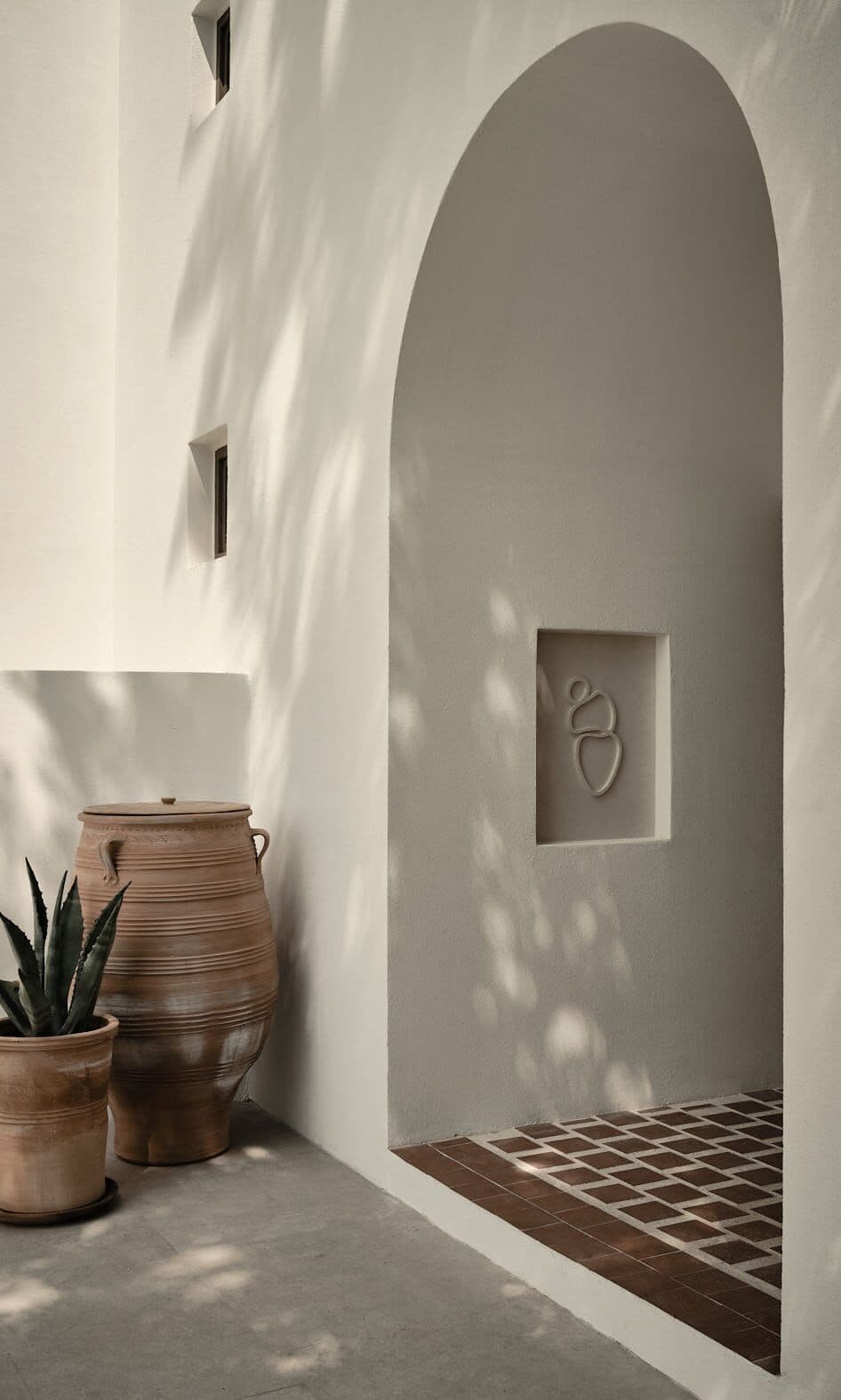 Parīlio Hotel, Europe — Whitewashed arched alcove with geometric tile floor, terracotta vessels, and minimalist Mediterranean architecture bathed in sunlight.