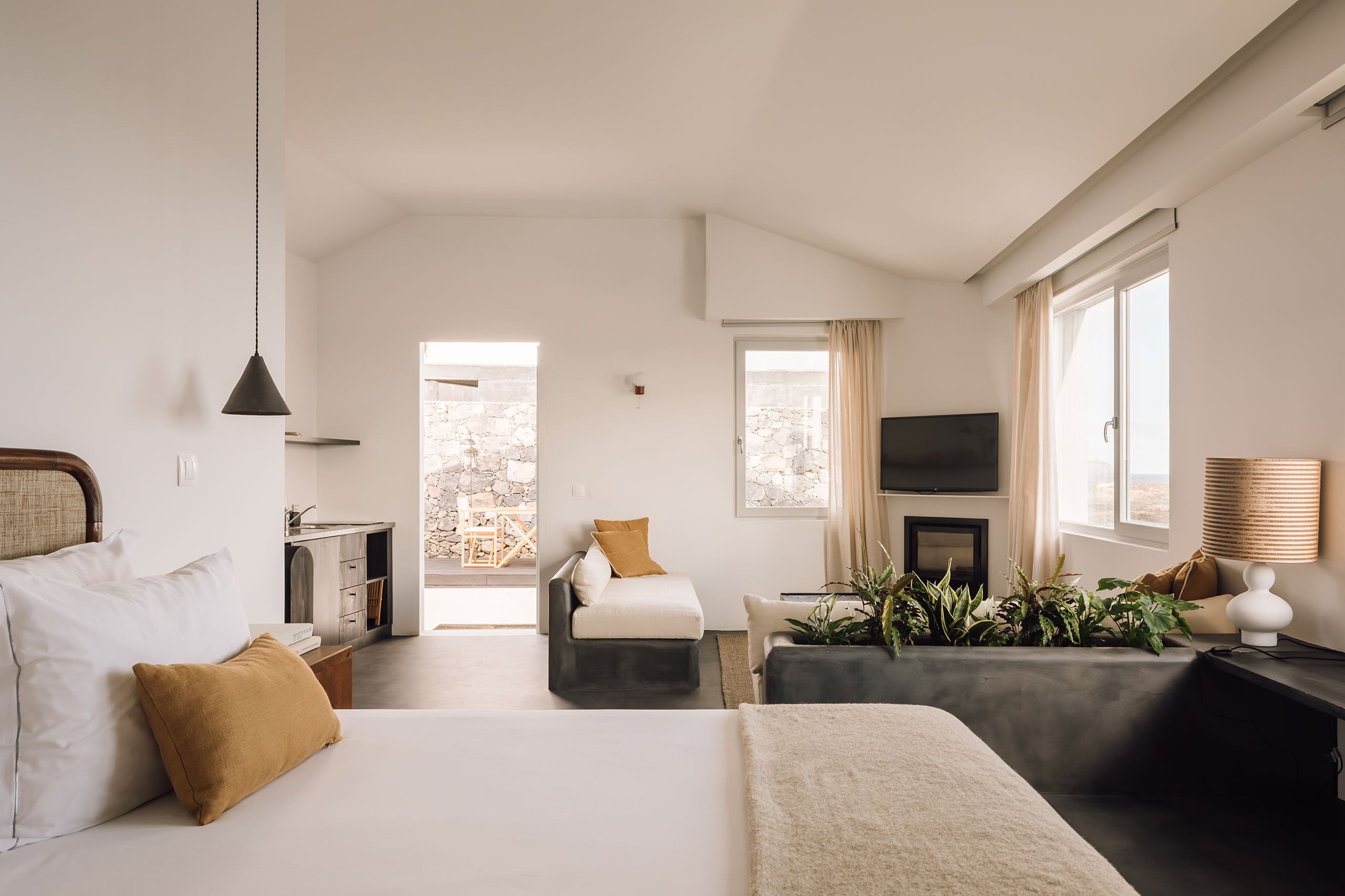 White Hotel, Europe — Minimalist studio suite with terracotta accents, fireplace, panoramic windows, and desert views, concrete and natural materials throughout.