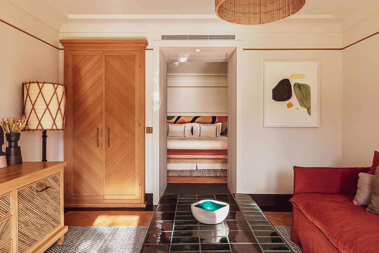 Hôtel Lou Pinet, Europe — Warm wood wardrobe, open walk-in closet, red velvet daybed, black tile floor, natural light, contemporary luxury bedroom.