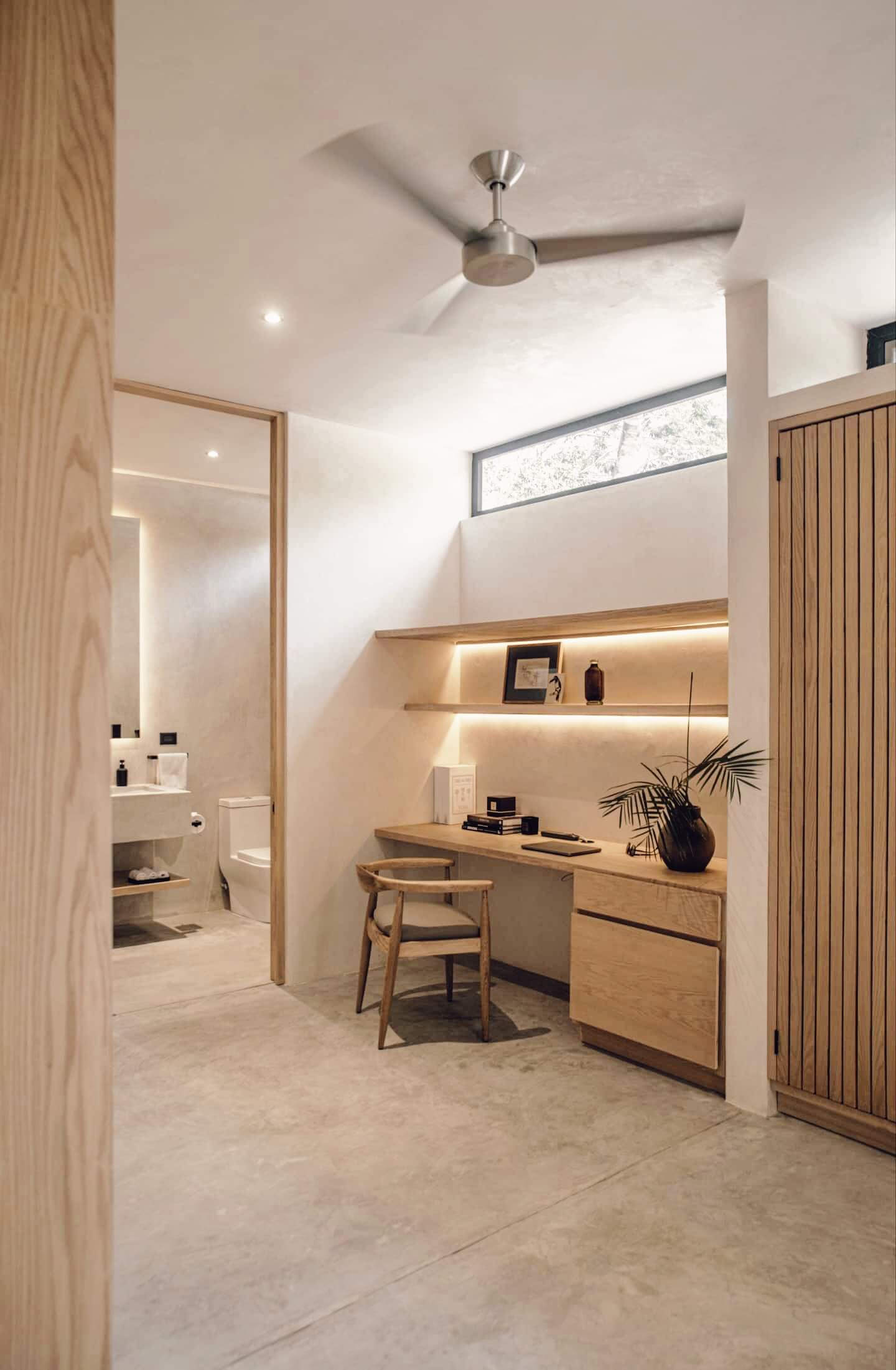 Villa Cava, Mexico — Minimalist ensuite with warm wood cabinetry, integrated lighting, marble flooring, and natural light from transom window.