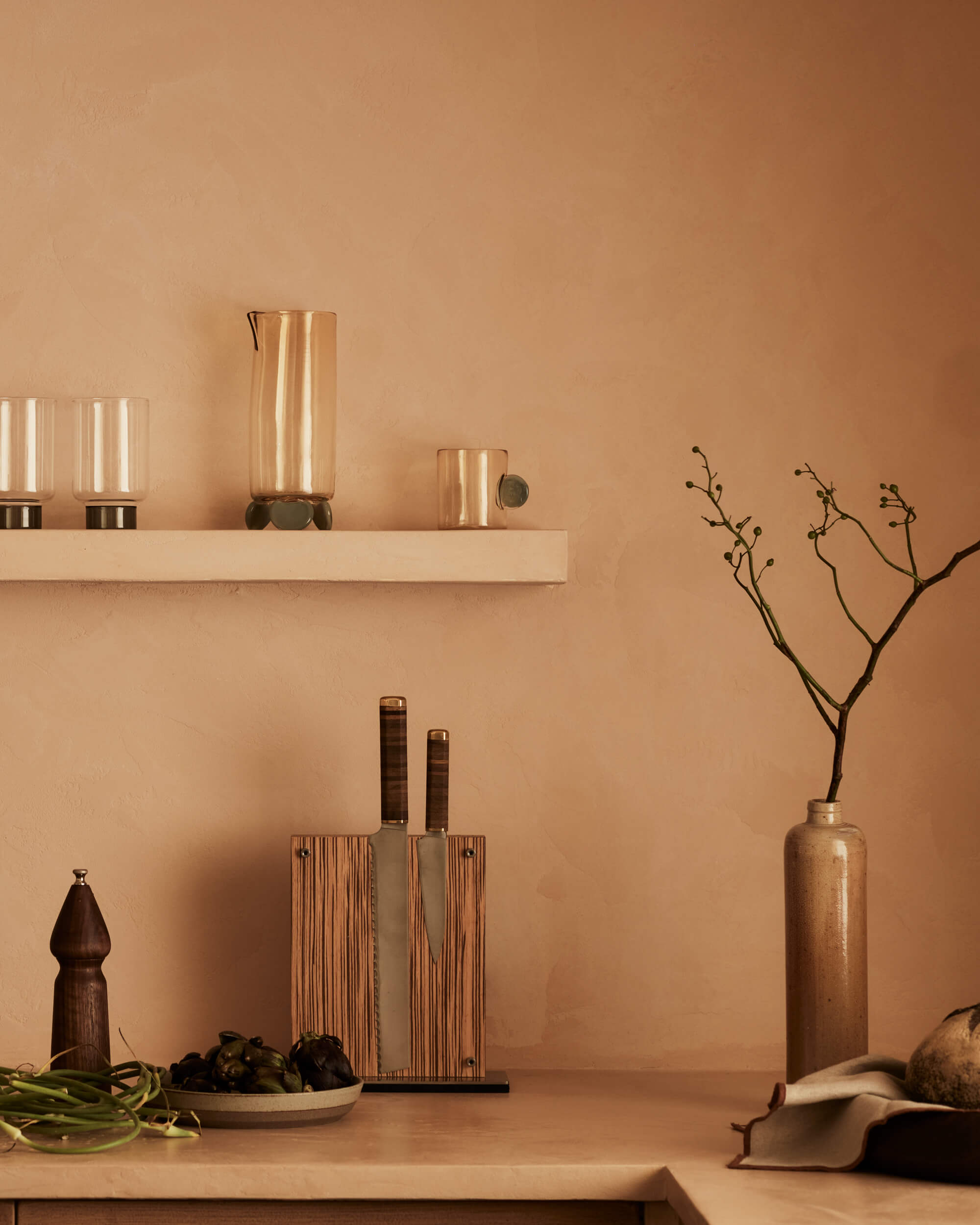 Arjé Home, North America — Minimalist kitchen styling with terracotta walls, brass vessels, wooden utensils, and dried botanicals in bronze vase.