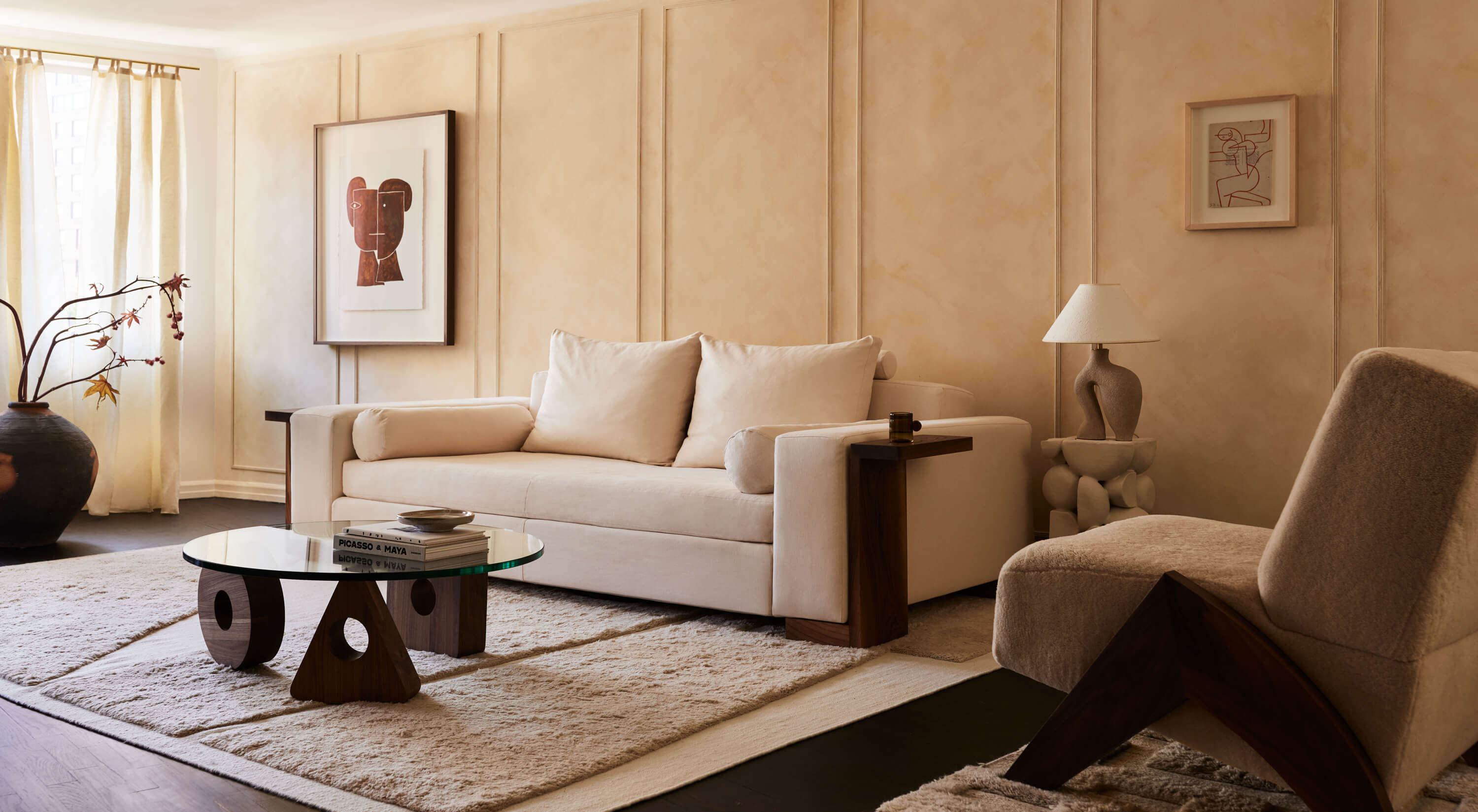 Arjé Home, North America — Minimalist living room with cream sofa, sculptural wooden coffee table, textured neutral palette, and framed abstract artwork.