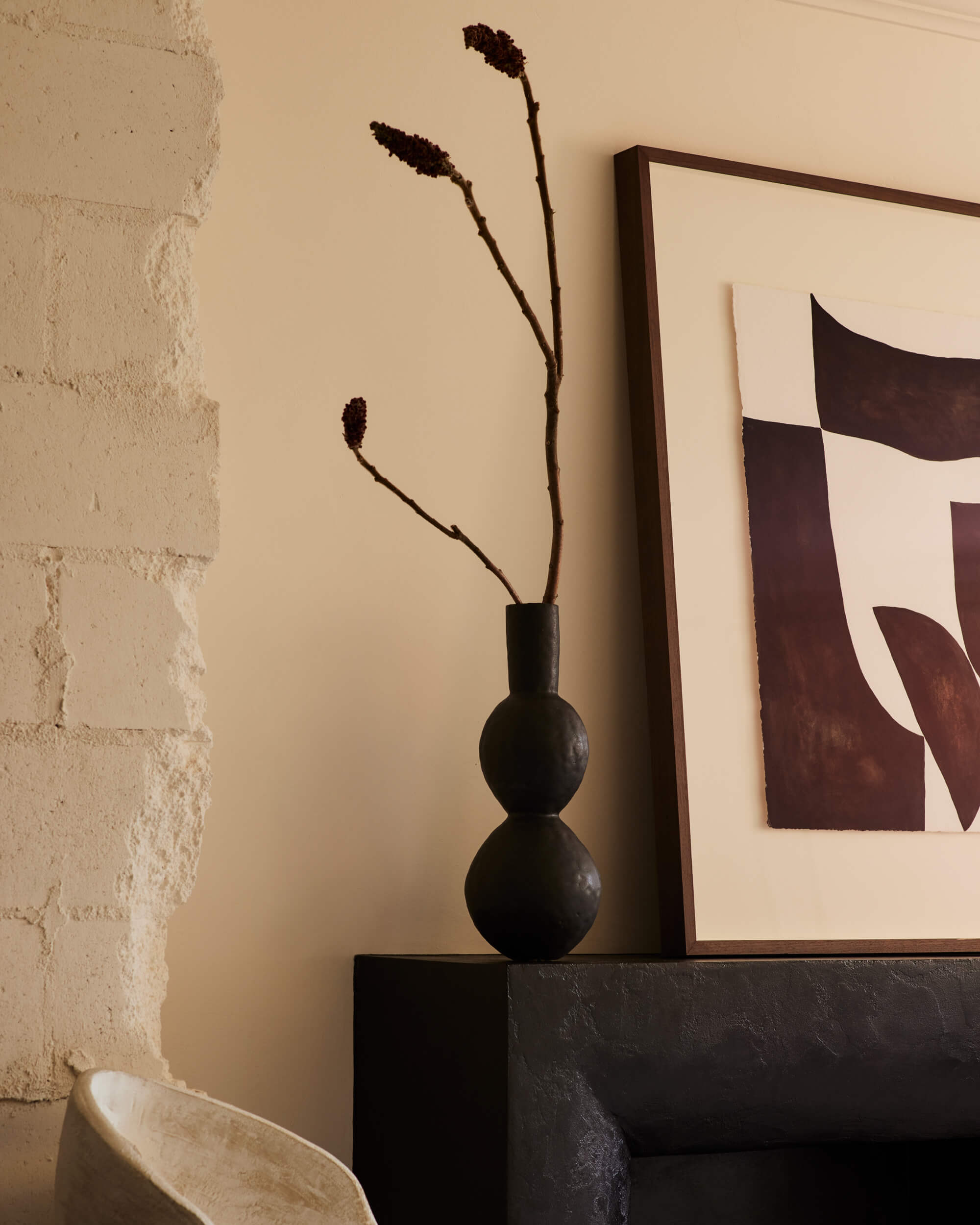 Arjé Home, North America — Dark ceramic vase with dried botanicals beside framed abstract artwork on textured wall, minimalist interior styling.