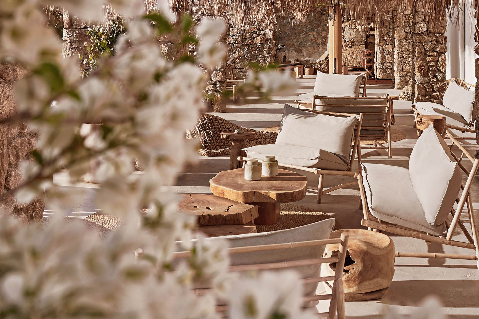 The Wild, Europe — Terracotta courtyard with wooden lounge chairs, white cushions, stone archways, and flowering vines in soft Mediterranean light.