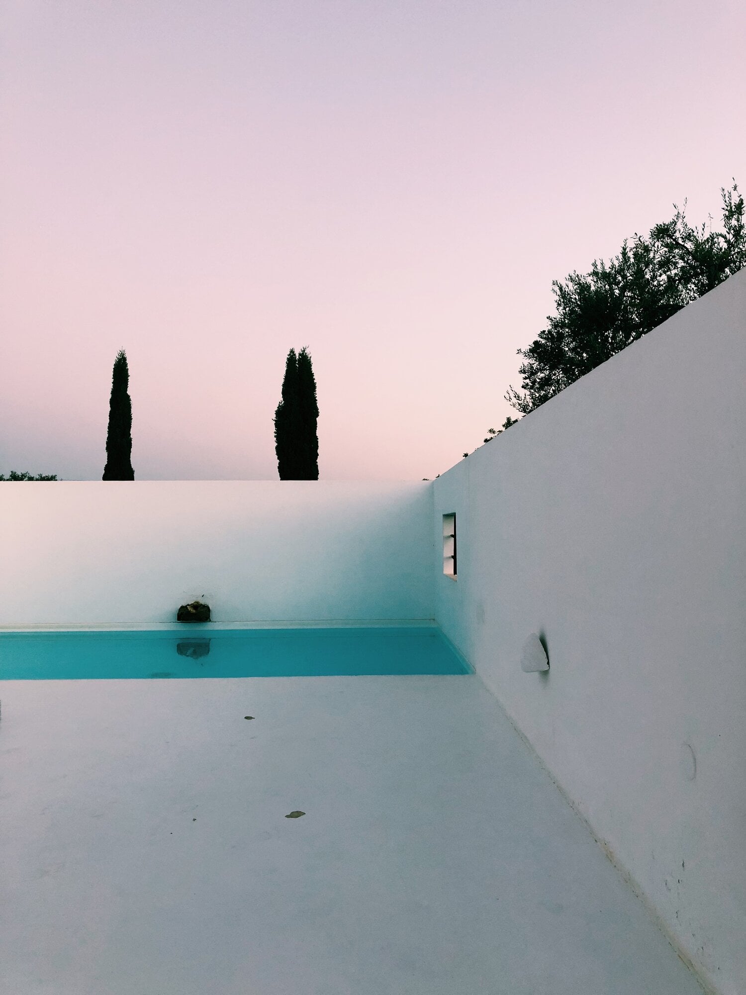 Pensão Agrícola, Europe — Minimalist poolside architecture with turquoise water, white walls, cypress trees, and soft twilight sky.