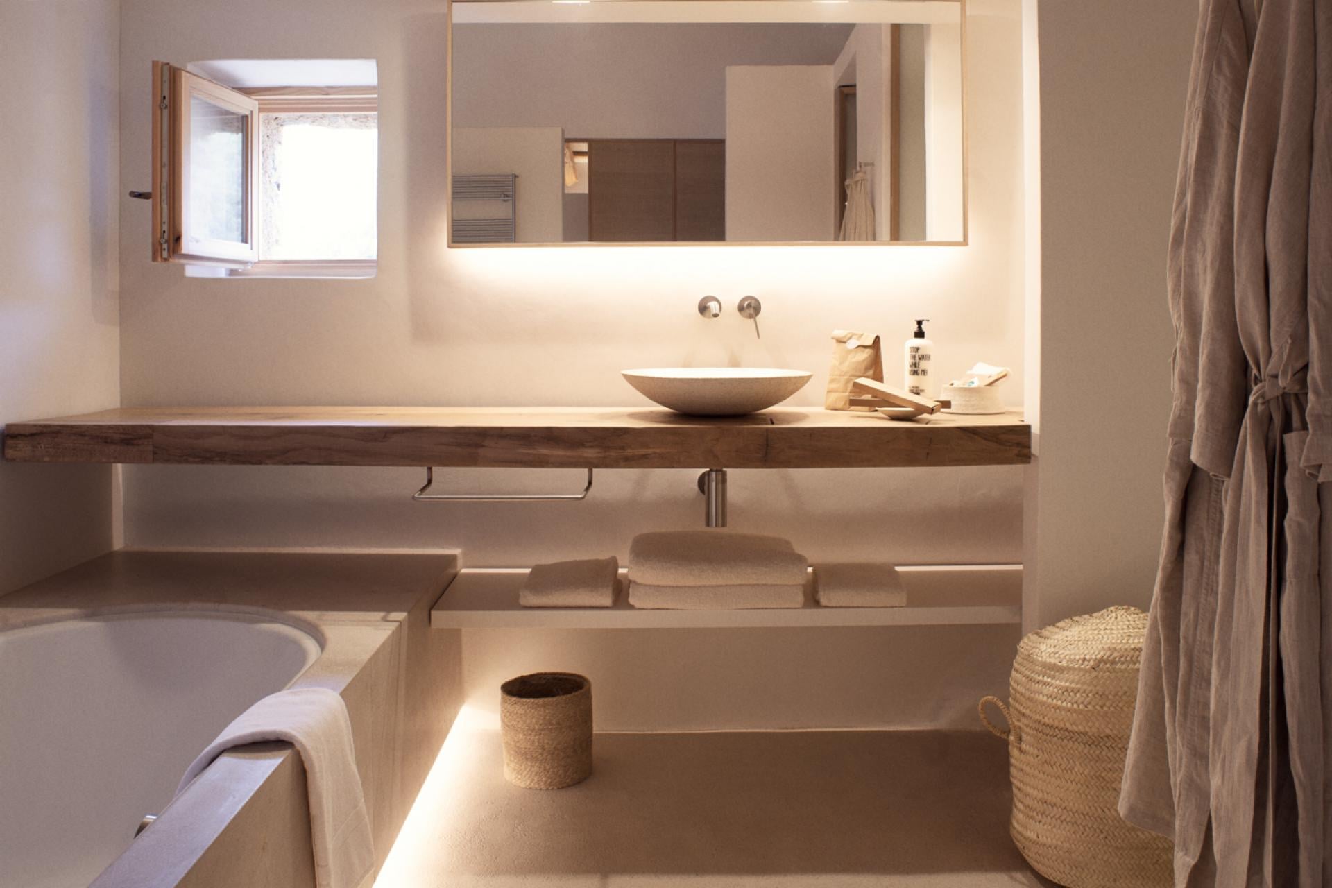 Es Racó d'Artà, Balearic Islands, Spain — Minimalist bathroom with warm limestone, vessel sink, backlit mirror, soaking tub, natural light, neutral textiles.