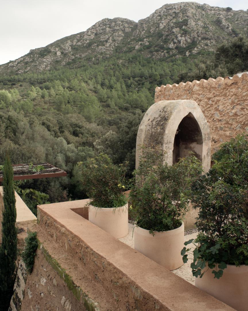 Es Racó d'Artà, Balearic Islands — Arched stone doorway in terracotta walls overlooking forested mountains and olive groves, Mediterranean minimalist architecture.
