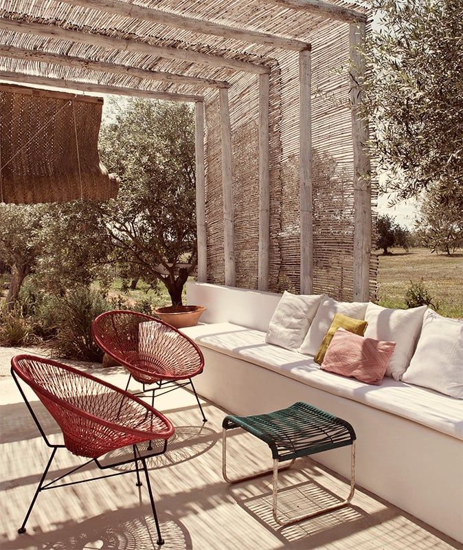 Pensão Agrícola, Europe — Pergola-shaded terrace with woven screens, red wire chairs, cream linen sofa, olive trees, and dappled sunlight across wooden deck.