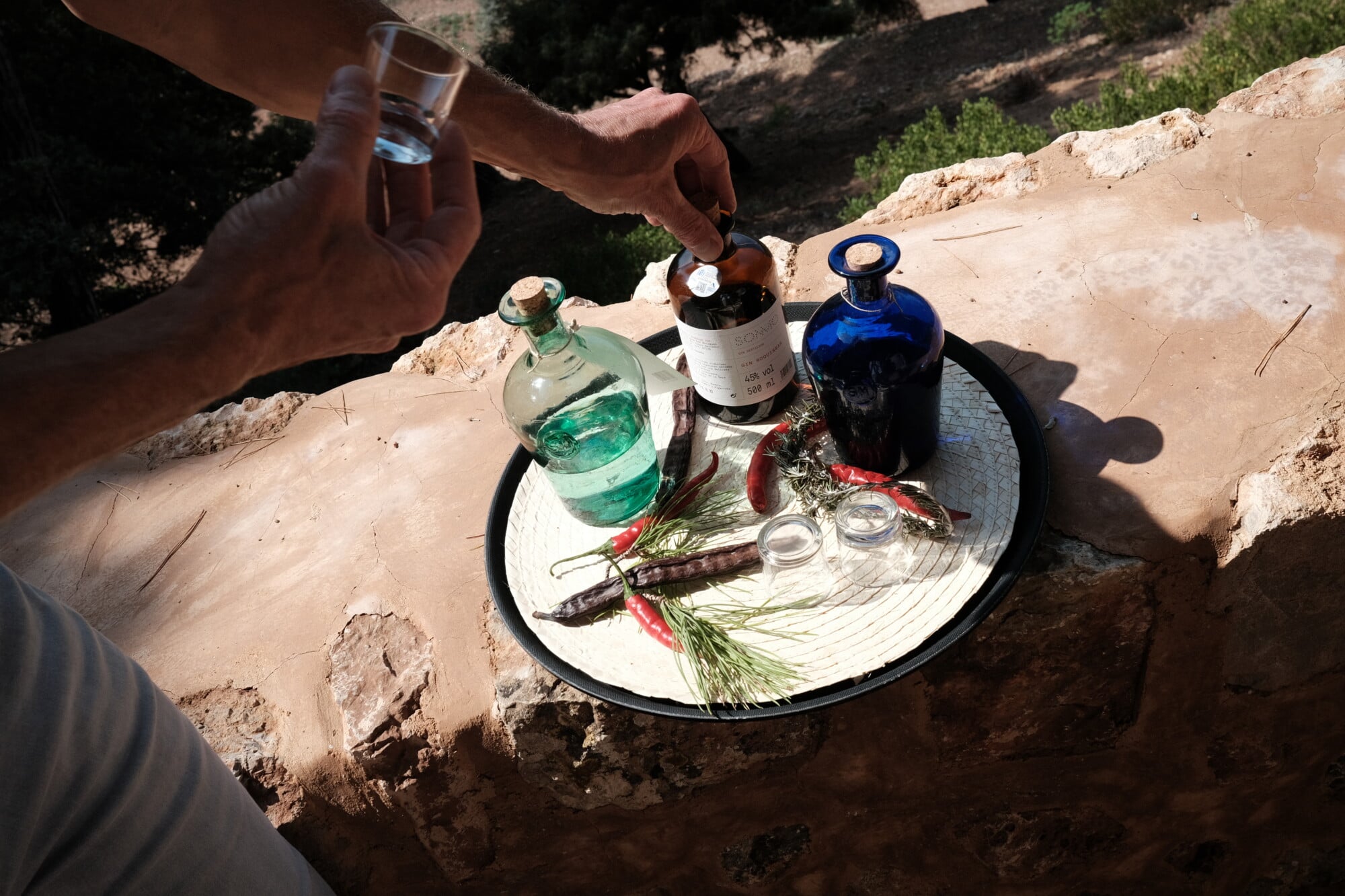 SONMO, Balearic Islands — Overhead view of natural ingredients and glass bottles arranged on white plate in sandy courtyard setting, Mediterranean culinary styling.