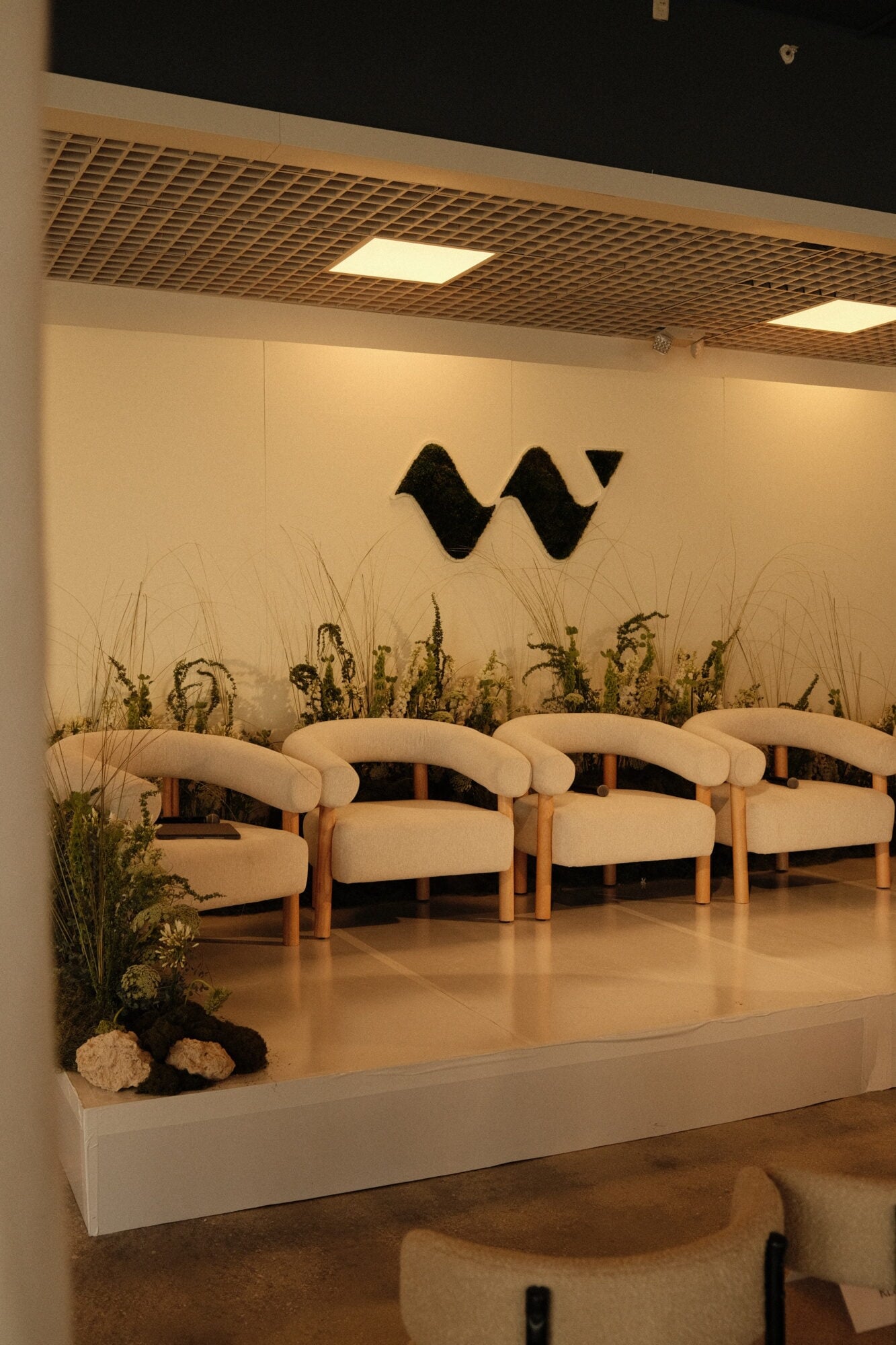 The New Frontier of High-Fidelity Hospitality — Modern hospitality lounge with cream sculptural chairs, dried botanical installations, black wavy wall art, and warm recessed lighting above polished concrete floor.