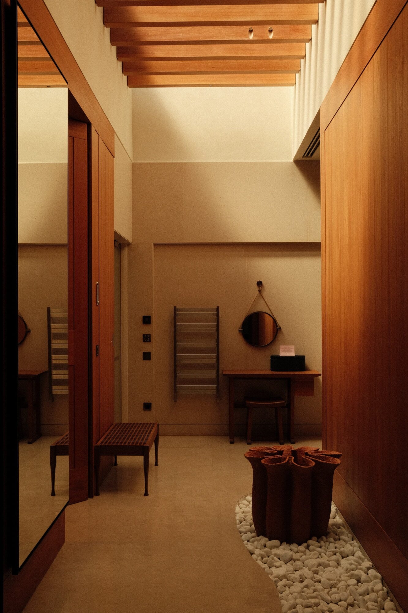 Mandarin Oriental Bodrum, Asia — Minimalist spa sanctuary with exposed wood beams, warm stone walls, timber furnishings, and white pebble accents creating serene wellness atmosphere.