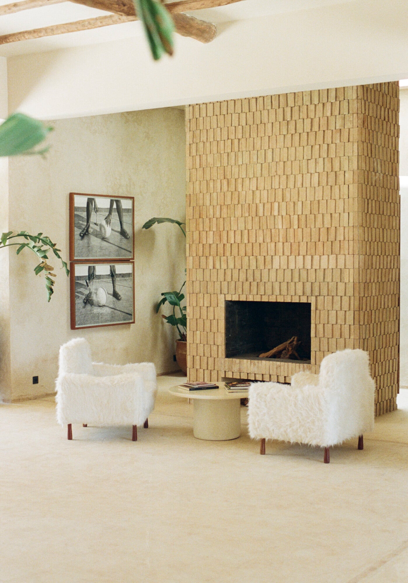 Farasha Farmhouse, Africa — Minimalist living room with cream brick fireplace, white sheepskin chairs, wooden beams, and potted plants in soft natural light.