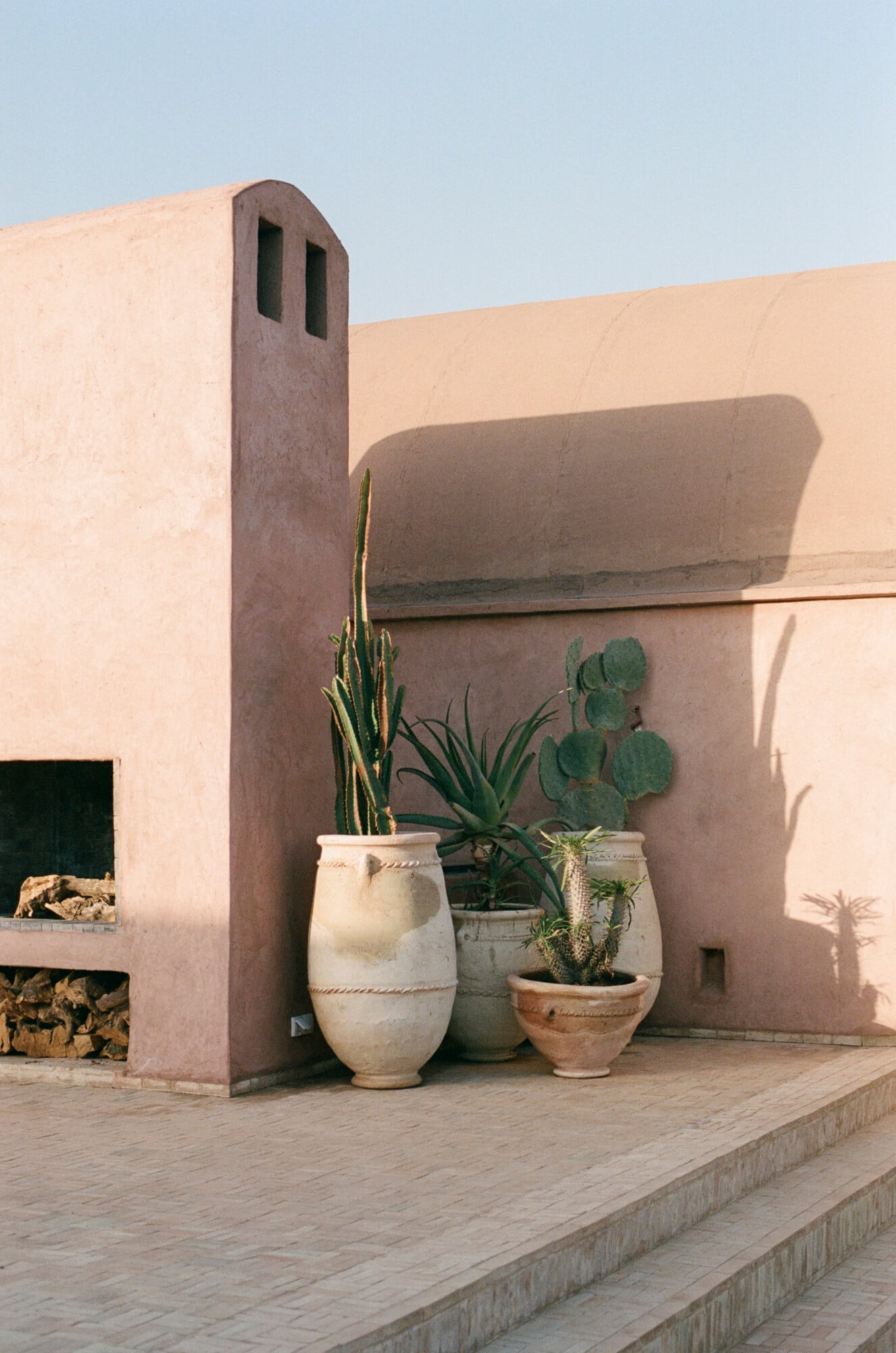 Farasha Farmhouse, Africa — Desert courtyard with clay barrel planters holding succulents and cacti, earthy adobe architecture casting geometric shadows under clear sky.
