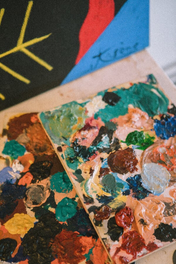 Fondation Vincent van Gogh Arles — Artist's wooden palette with vibrant oil paint daubs in green, blue, red, orange and yellow, displayed with colorful abstract artwork above.