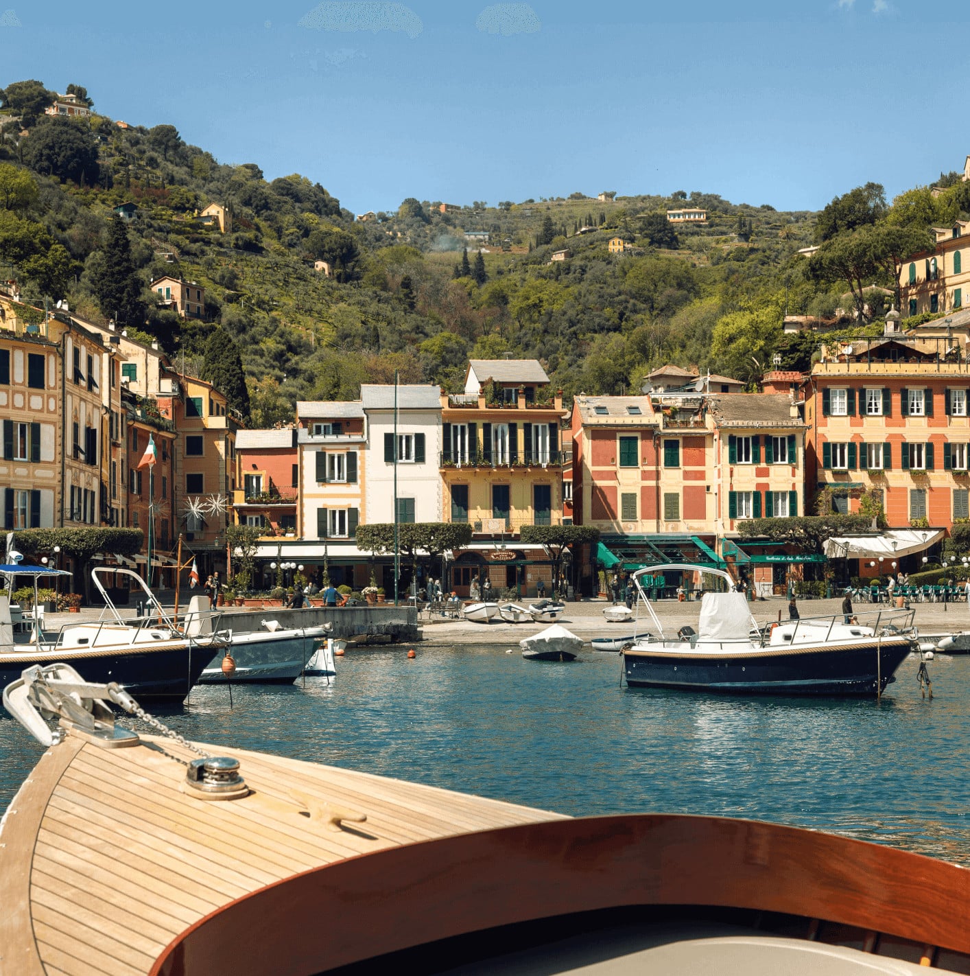 Gozzo Tour, Europe — Pastel waterfront buildings with wooden fishing boats moored in turquoise Mediterranean harbor, hillside village backdrop, afternoon light.
