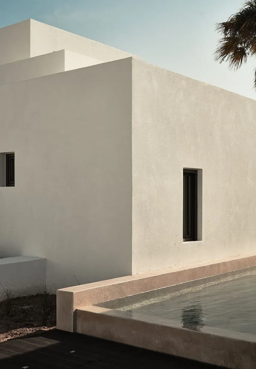 Parīlio Hotel, Europe — Minimalist white concrete architecture with narrow vertical windows, reflecting pool, and palm tree against clear sky.