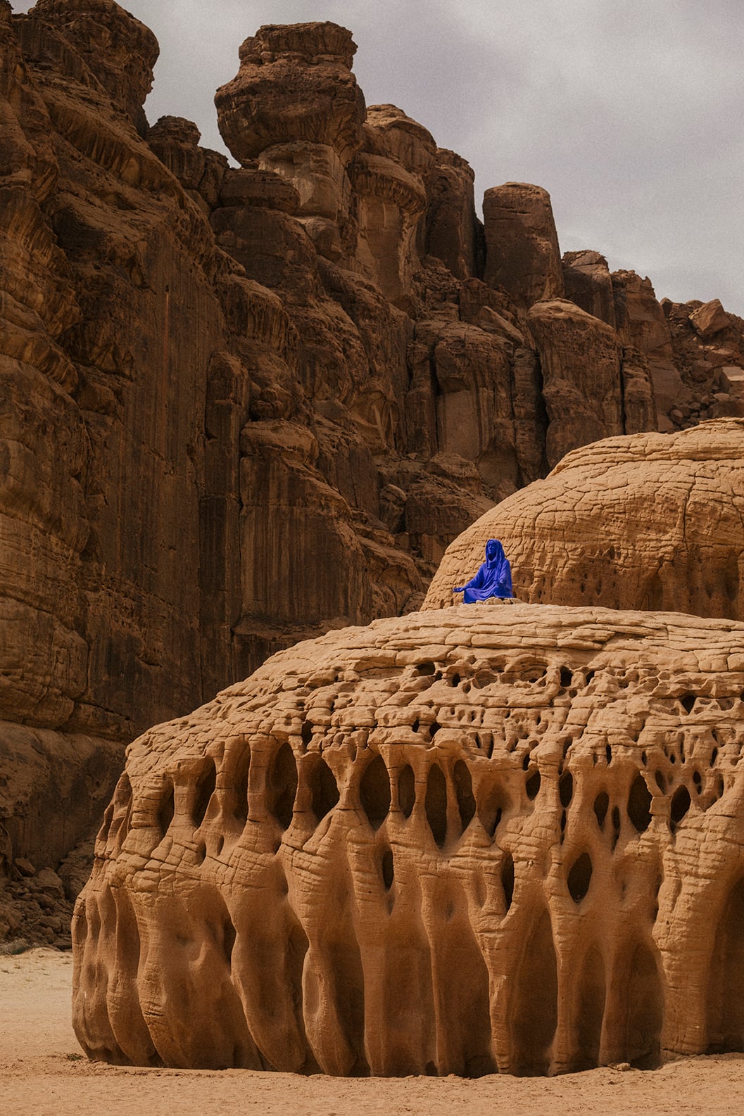 Elyseria by Lita Albuquerque — Figure in cobalt blue sitting atop carved sandstone formation amid ancient rock monuments and desert landscape.