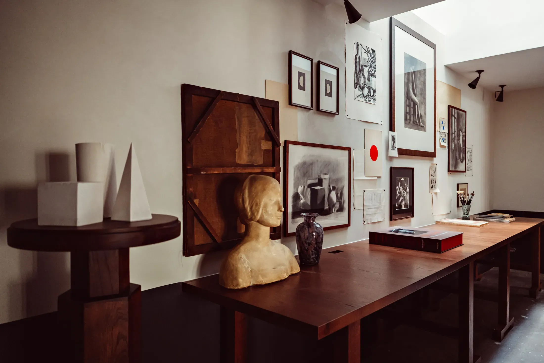 Académies et des Arts, Europe — Gallery space with dark wood display tables, sculptural busts, framed artwork, and modernist ceramics under gallery lighting.