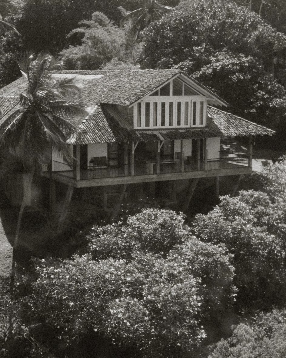 Kurulu Bay, Asia — Stilted wooden villa with pitched roof and slatted railings nestled among lush tropical vegetation, black and white architectural photography.