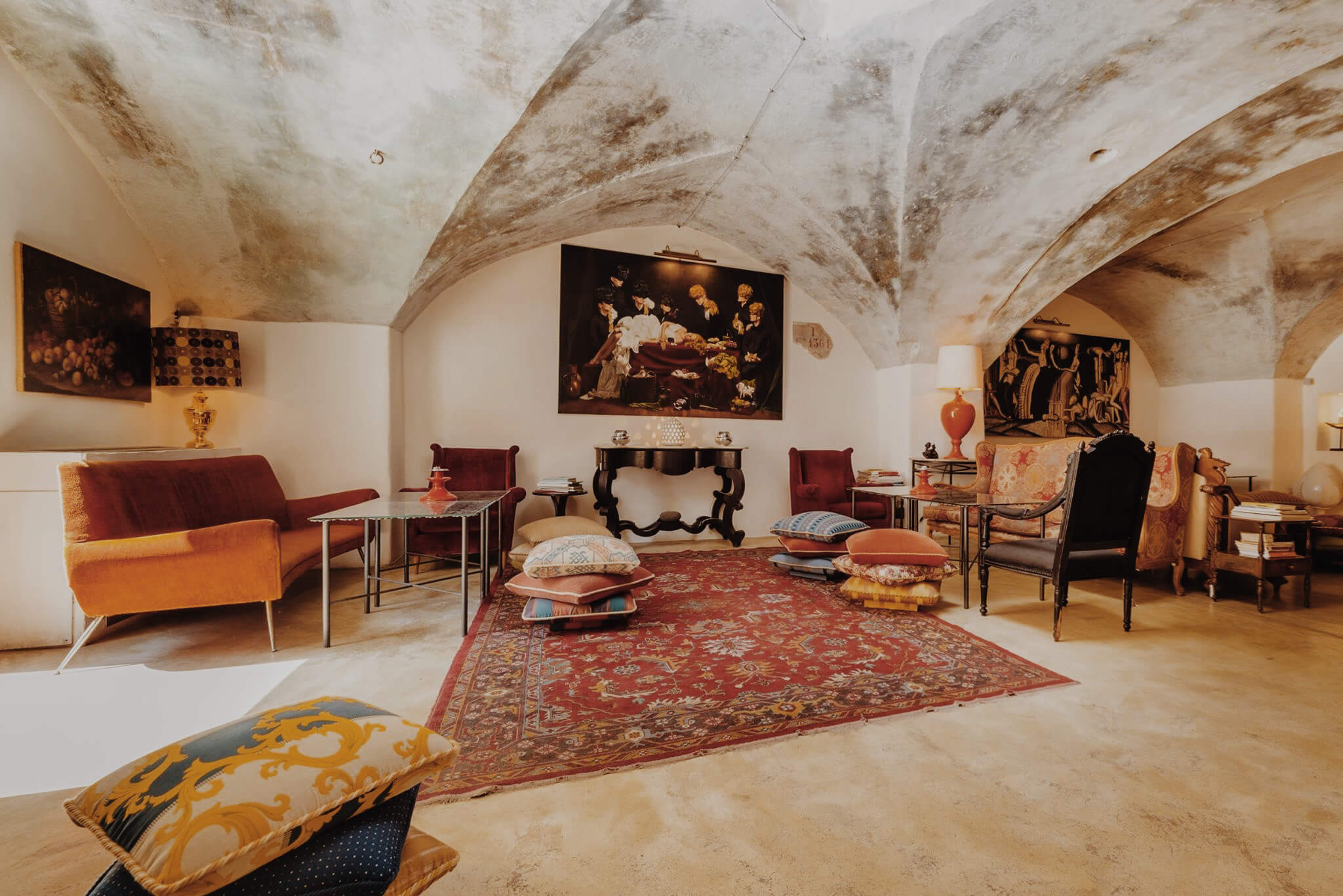 Blanc Gallipoli, Italy — Arched stone ceiling with terracotta details, mid-century furniture, red oriental rug, and classical artworks in luxury hospitality lounge.