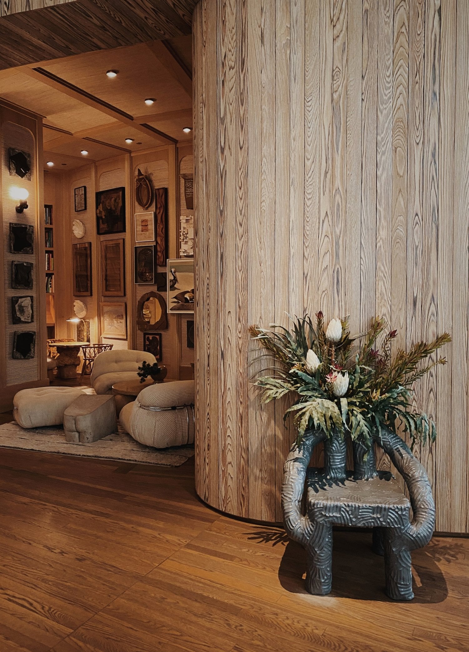 Santa Monica Proper, North America — Sculptural wooden vessel planter with dried flowers beside whitewashed wood-paneled gallery entrance, warm ambient lighting throughout luxury hospitality interior.