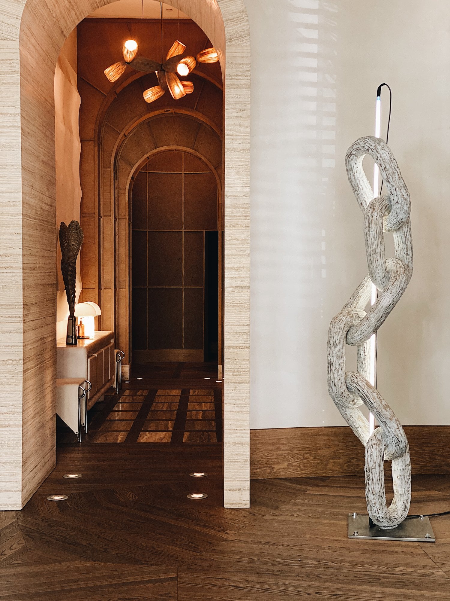 Santa Monica Proper, North America — Whitewashed sculptural chain link wall art beside warm wood archway with modern lighting fixtures and dark tile flooring.