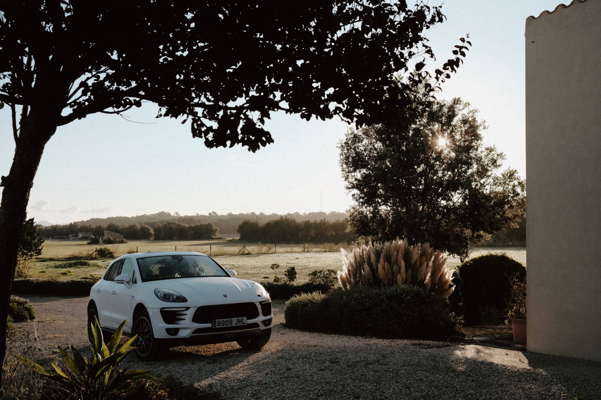 Eleven Pro Car Rental, Balearic Islands, Spain — White luxury SUV parked on gravel drive beside modern architecture, rural landscape with trees and open fields beyond.