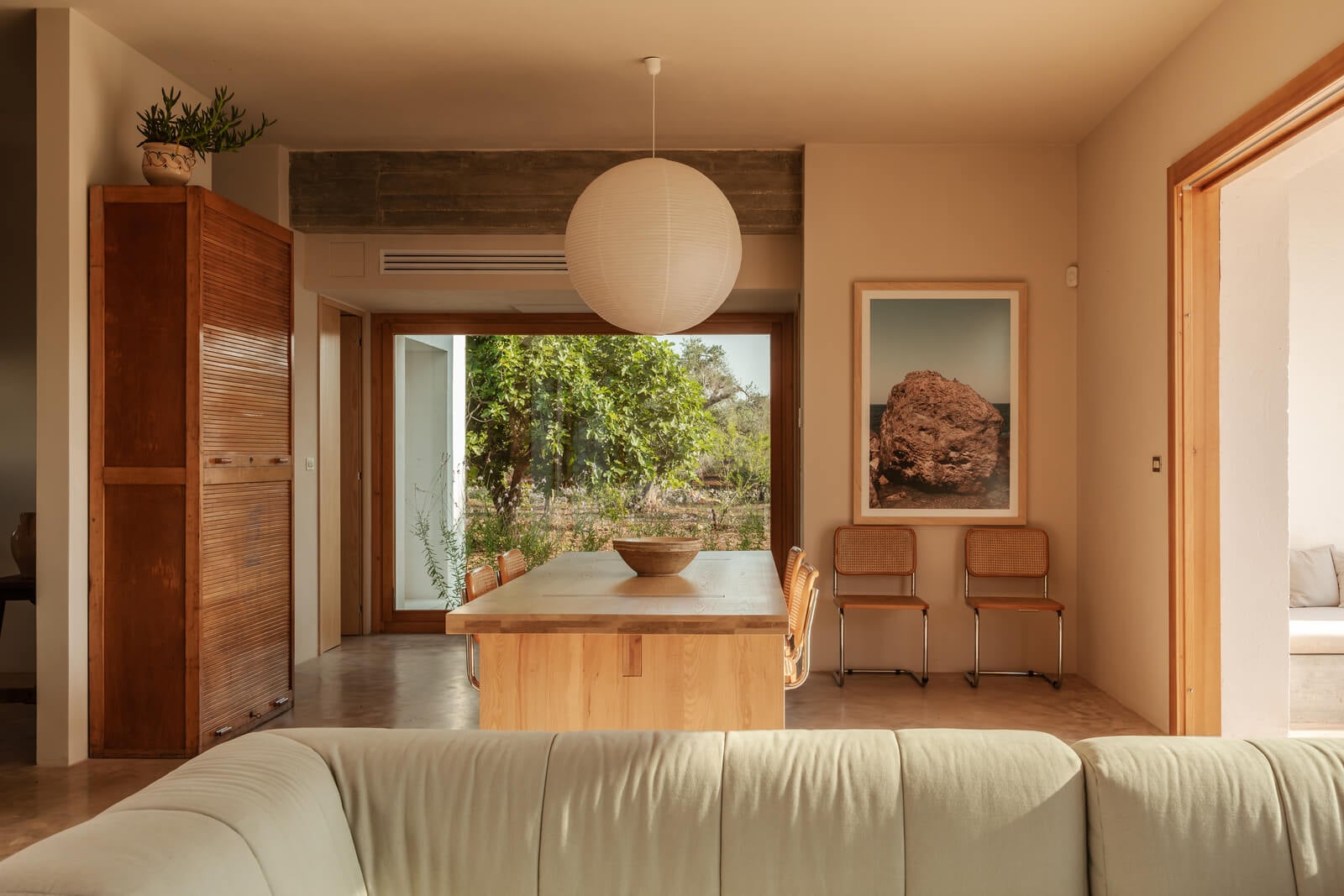 Casanguilla, Europe — Minimalist living room with terracotta walls, wooden furniture, pendant lighting, and garden views through floor-to-ceiling doors.