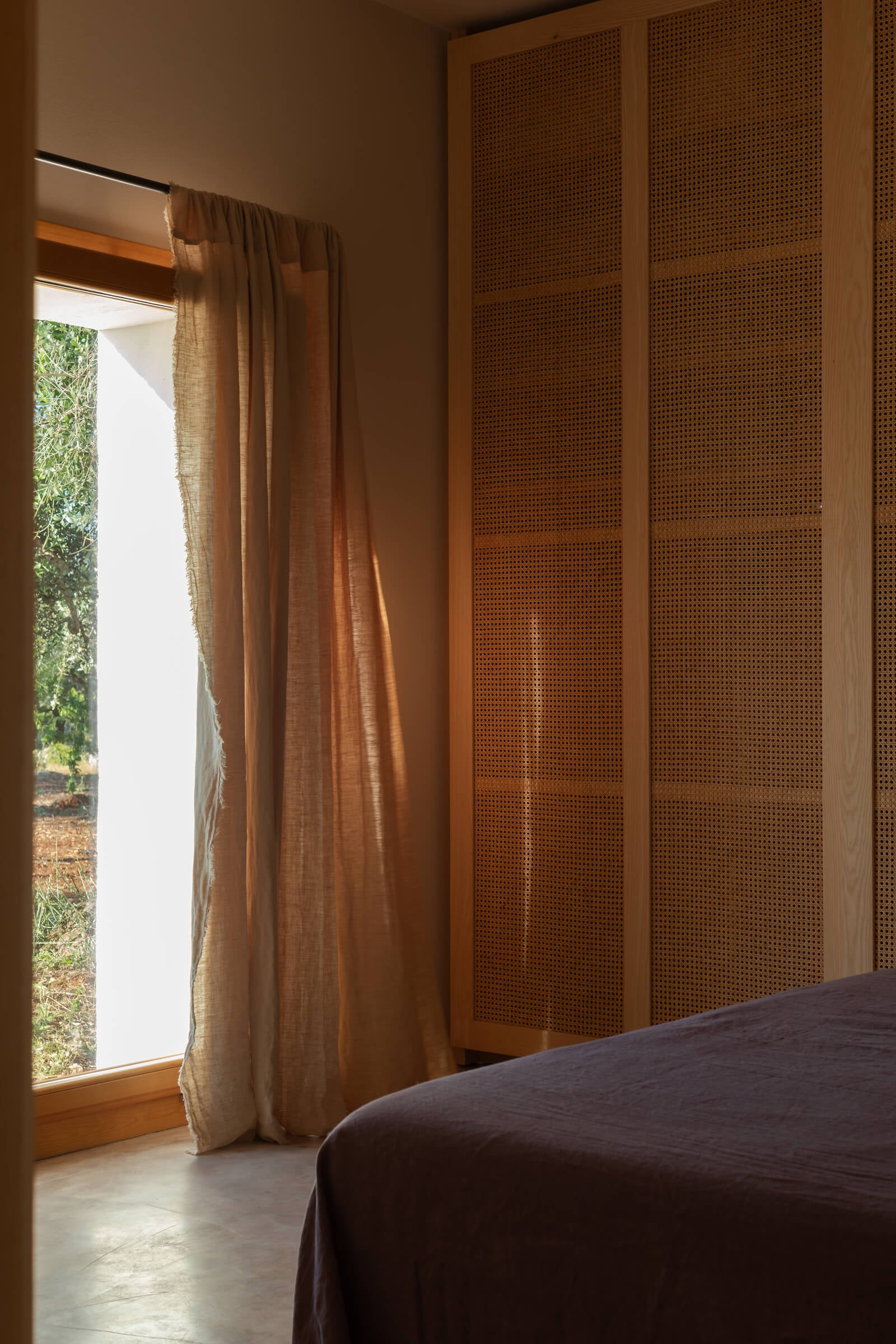 Casanguilla, Europe — Minimalist bedroom with perforated wood wardrobe, linen curtains, and natural light from garden-facing window.