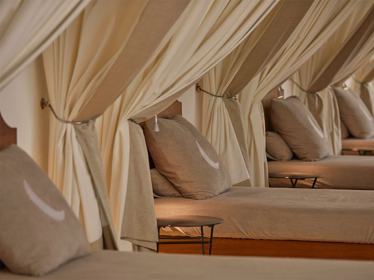 Cap Rocat, Balearic Islands — Cream linen canopy beds with natural wood frames and neutral pillows in minimalist luxury bedroom alcoves.