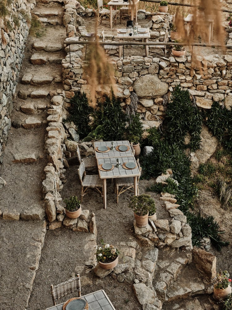 Raw, Europe — Aerial view of rustic stone courtyard with intimate dining setup, terra cotta planters, olive trees, and weathered limestone walls.