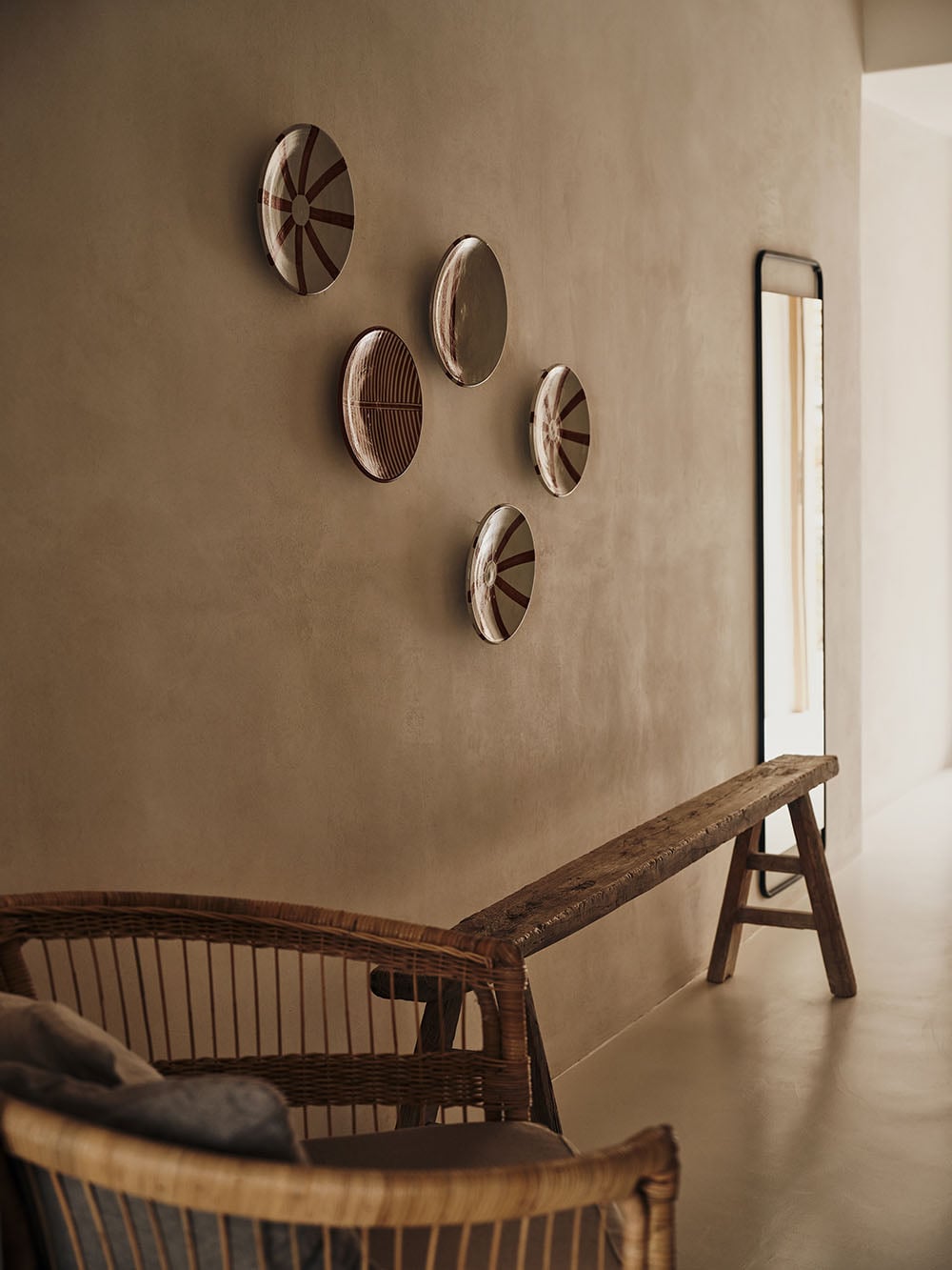 The Wild, Europe — Minimalist gallery wall with five woven ceramic wall hangings above wooden furniture in neutral interior with natural light.