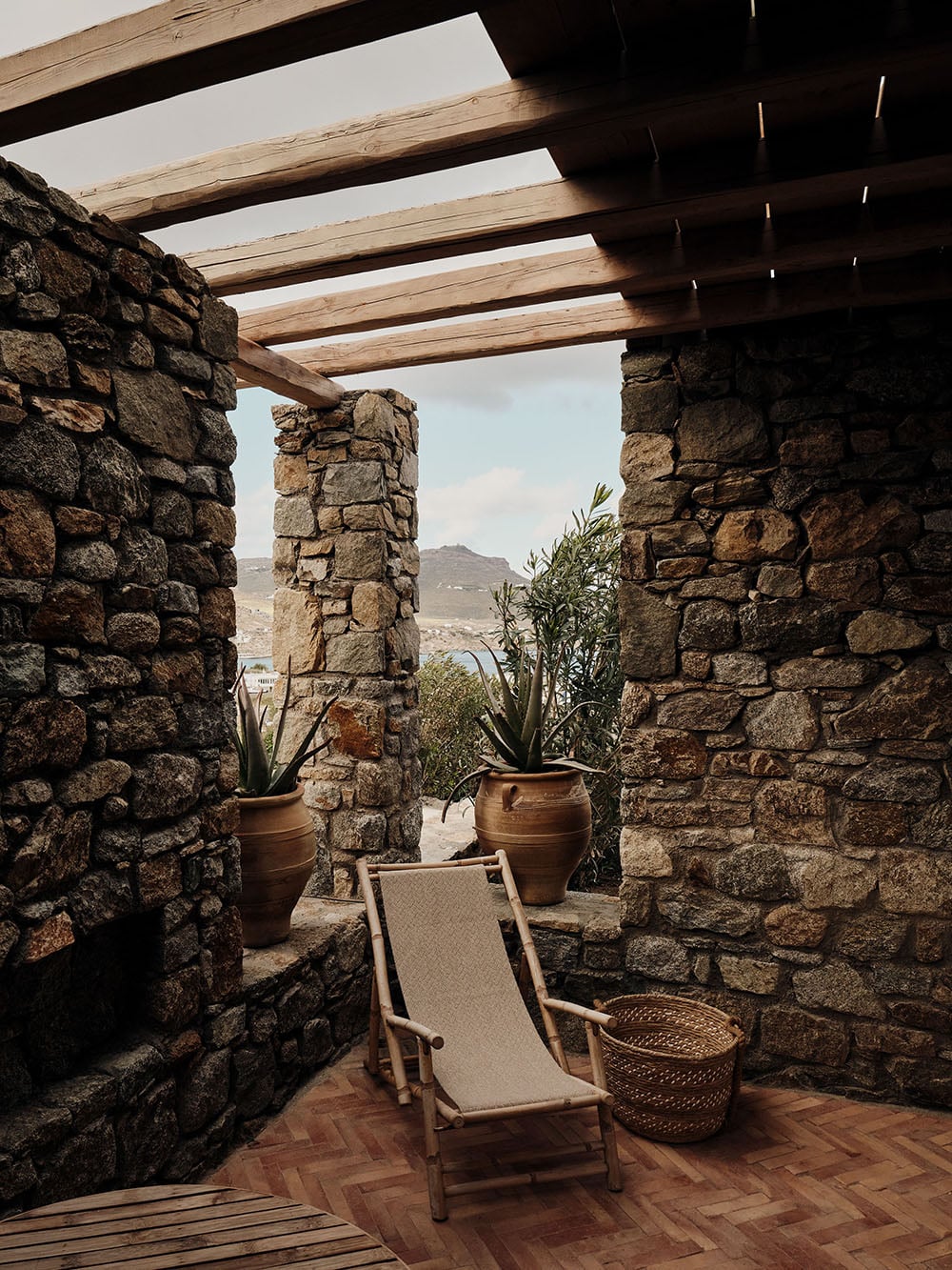 The Wild, Europe — Stone terrace with wooden pergola, terra cotta planters, canvas lounger, and mountain views at luxury hospitality design studio.