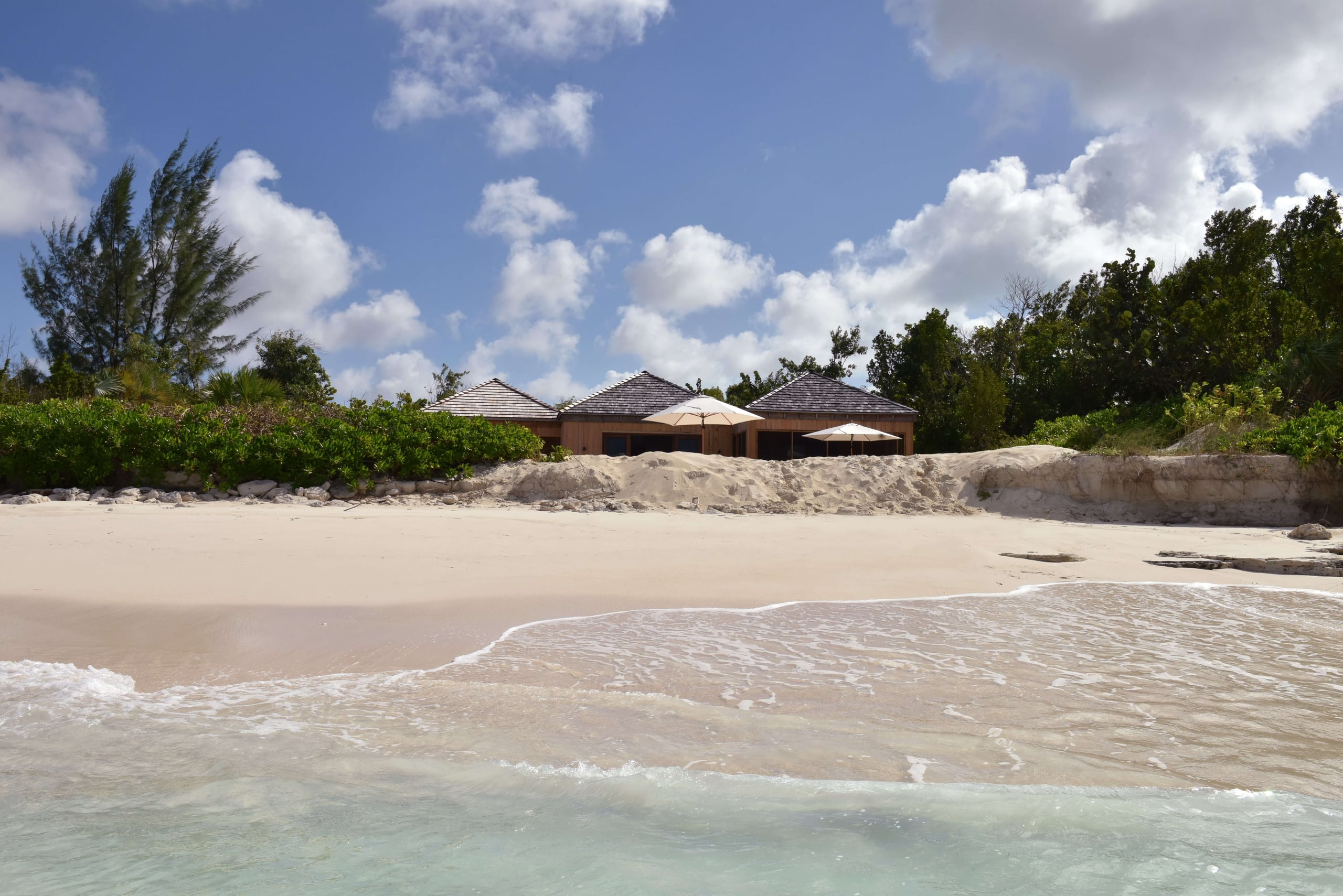 COMO Parrot Cay, North America — Beachfront wooden pavilions with white umbrellas, pristine sand, turquoise waters, and lush tropical vegetation under blue sky.